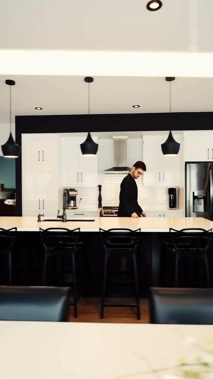 Modern kitchen with white cabinets, black island, pendant lights, and a man standing behind the counter.