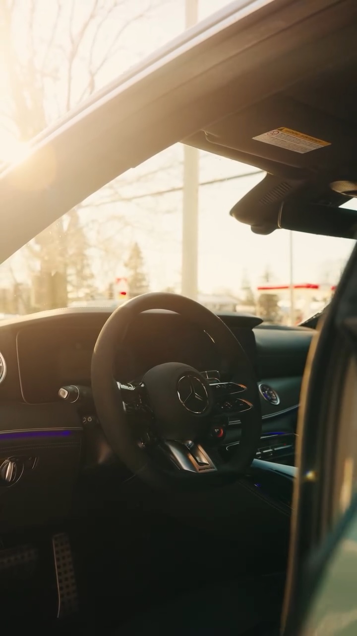 Interior of a Mercedes-Benz car showing steering wheel and dashboard in warm sunlight.