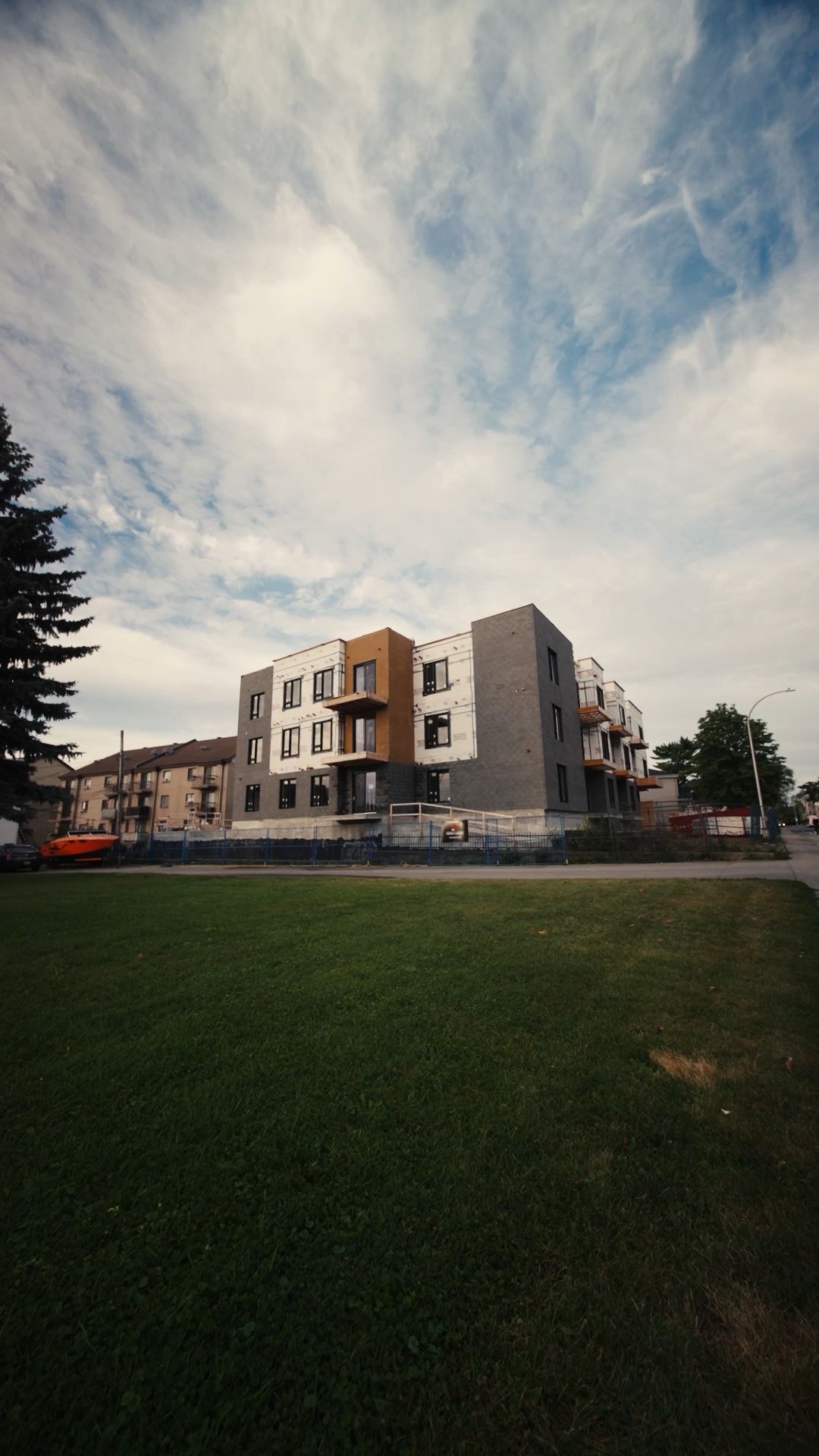 Modern three-story building under construction with green lawn and partly cloudy sky.