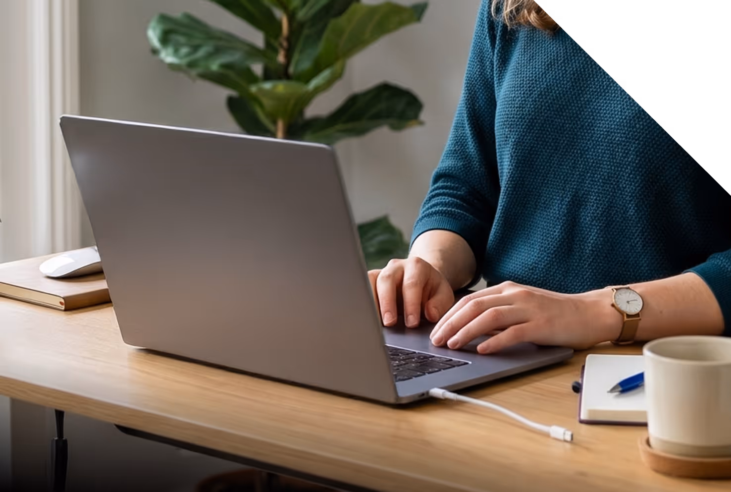 Person tapant sur un ordinateur portable posé sur un bureau en bois avec une tasse et un carnet.
