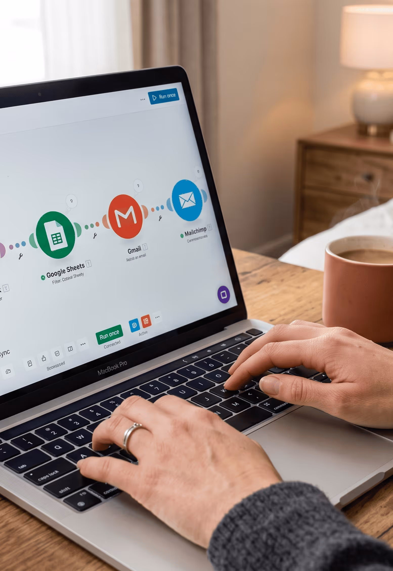 Person typing on MacBook Pro showing workflow with Google Sheets, Gmail, and Mailchimp icons on screen.