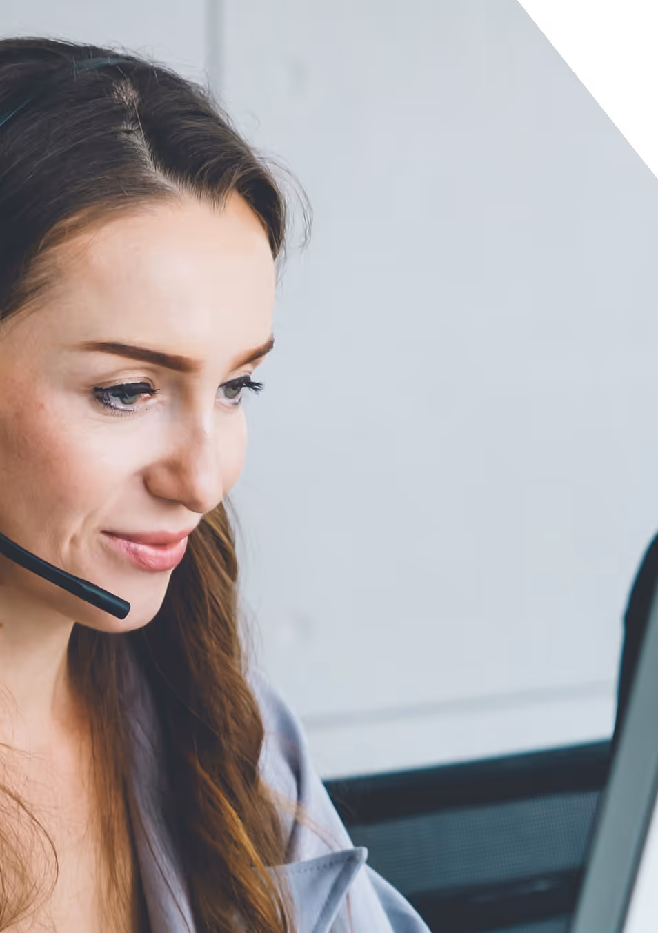 Femme souriante avec casque micro travaillant devant un ordinateur dans un bureau lumineux.