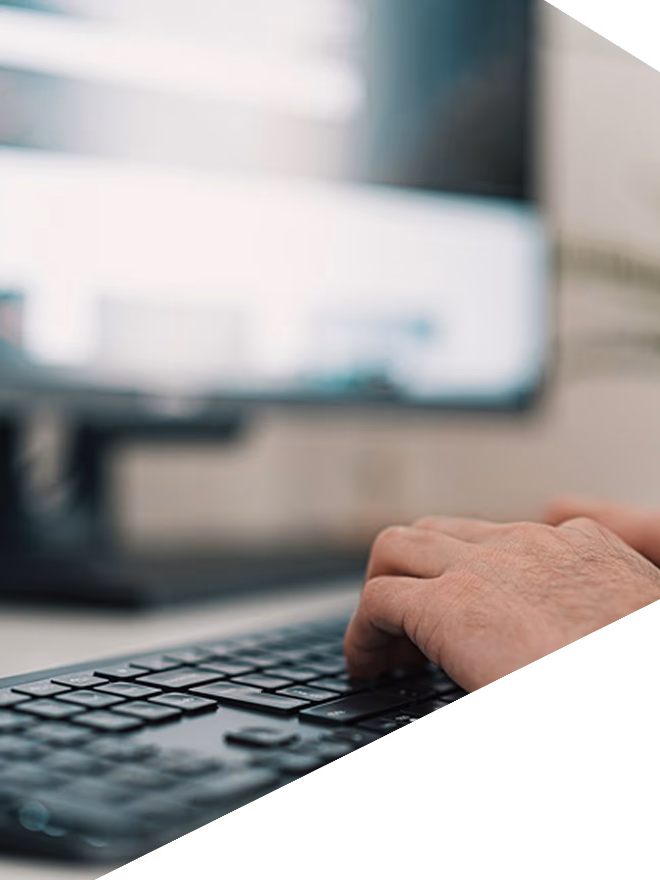 Main d'une personne tapant sur un clavier d'ordinateur avec un écran flou en arrière-plan.