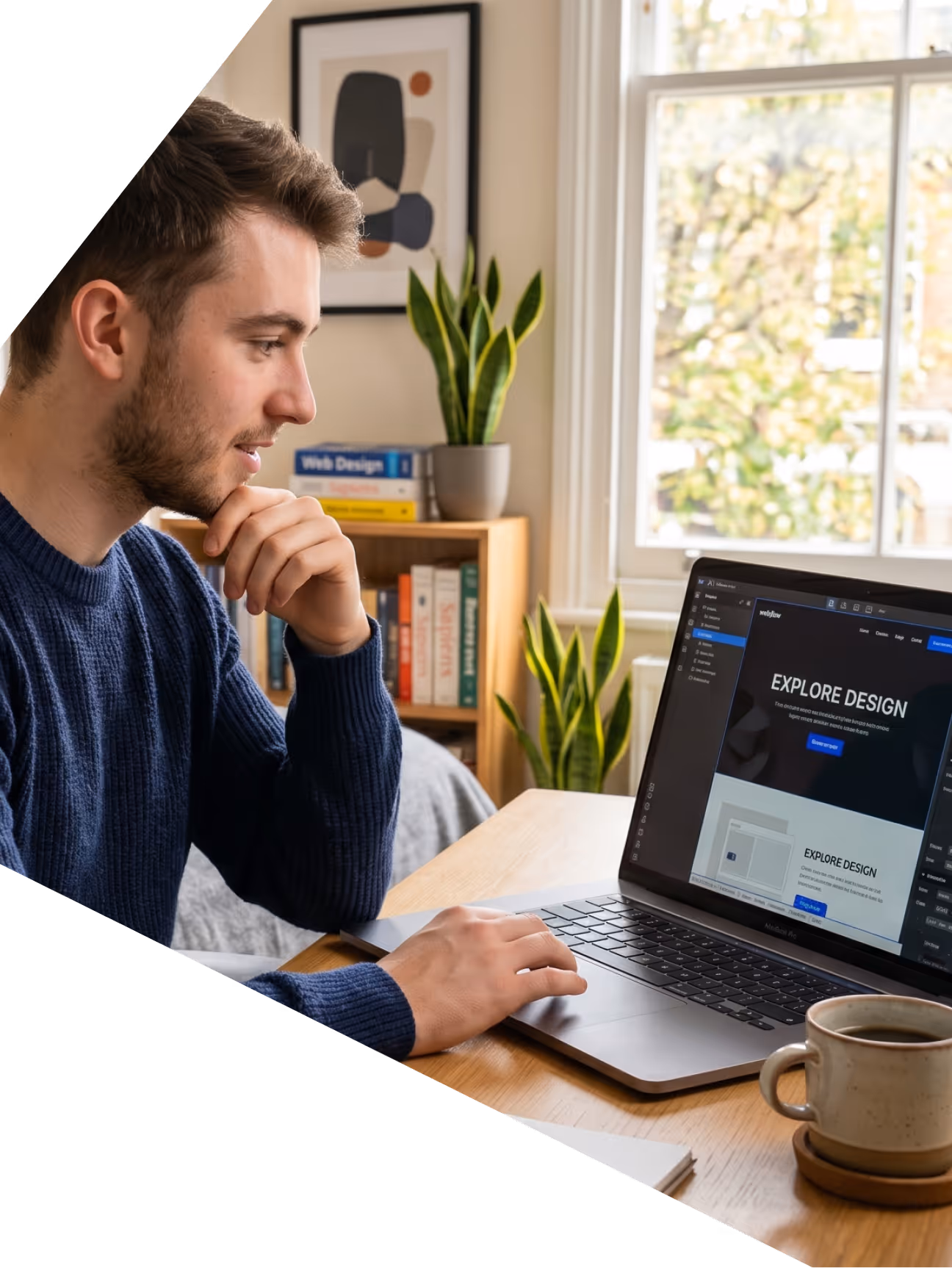 Un homme travaillant sur un ordinateur portable affichant une page de design, avec une tasse et plantes près.