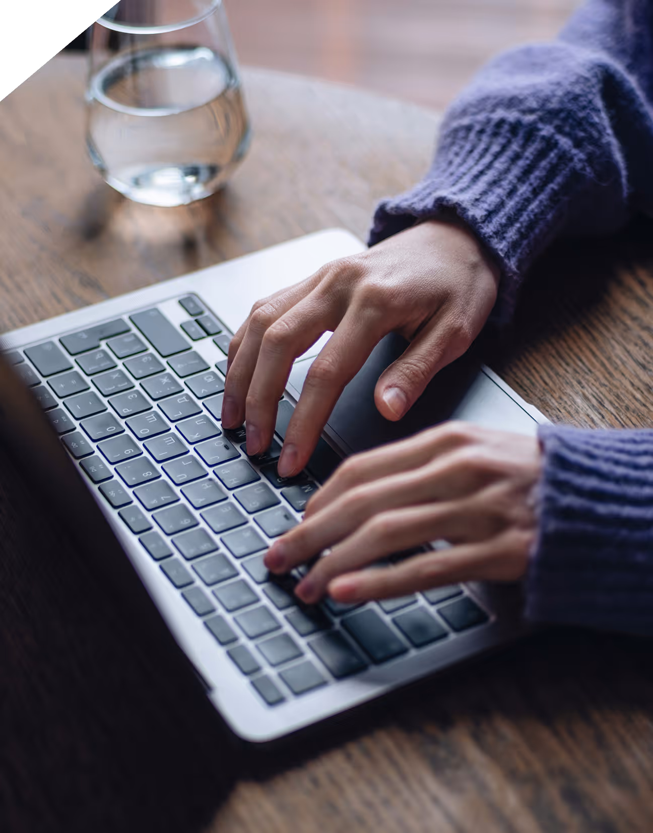 Deux mains tapant sur un clavier d’ordinateur portable posé sur une table en bois.