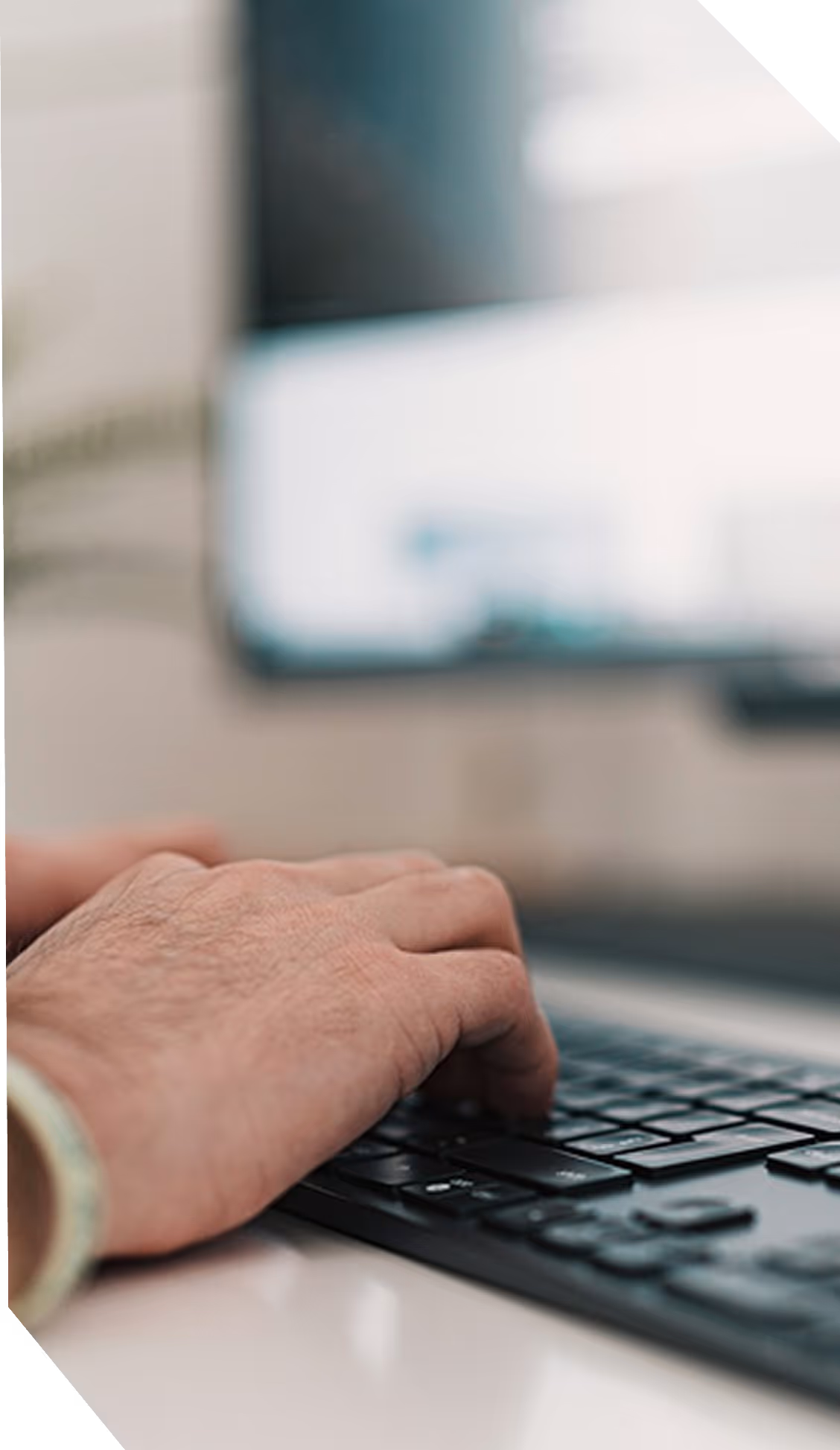 Main tapant sur un clavier d'ordinateur noir à côté d'un écran d'ordinateur flou.
