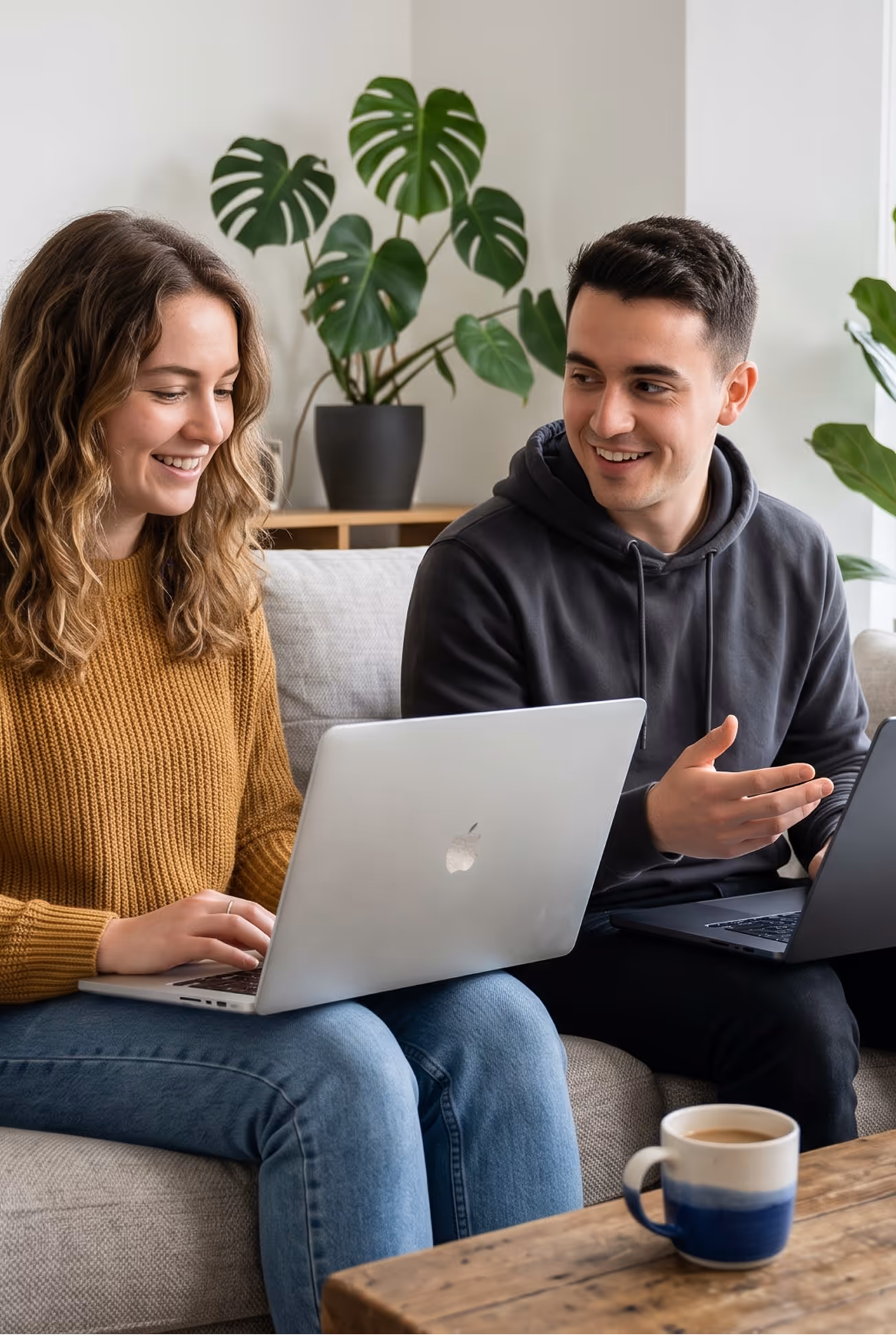 Un homme et une femme souriants utilisant des ordinateurs portables assis sur un canapé.