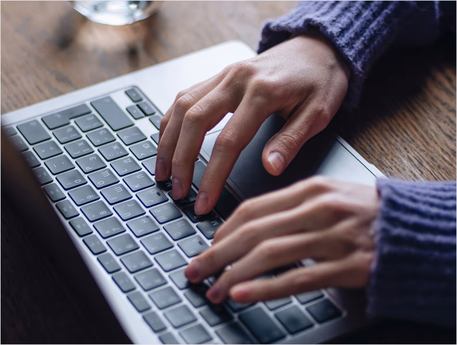Mains d'une personne tapant sur un clavier d'ordinateur portable sur une table en bois.