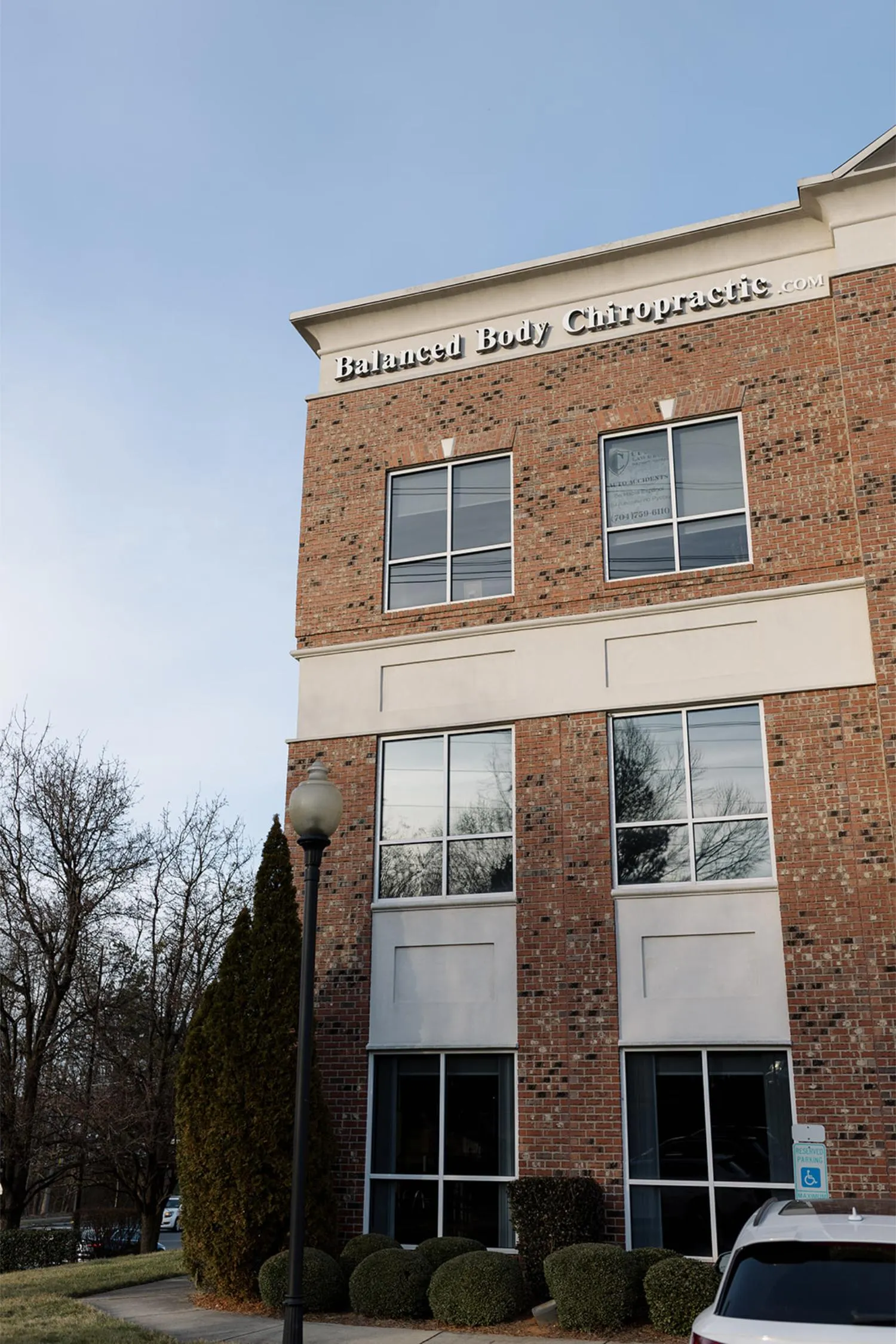 Brick office building with 'Balanced Body Chiropractic' sign and a parked white car outside.