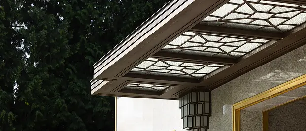 Modern glass canopy with geometric patterns over entrance attached to a building wall with a large lantern.
