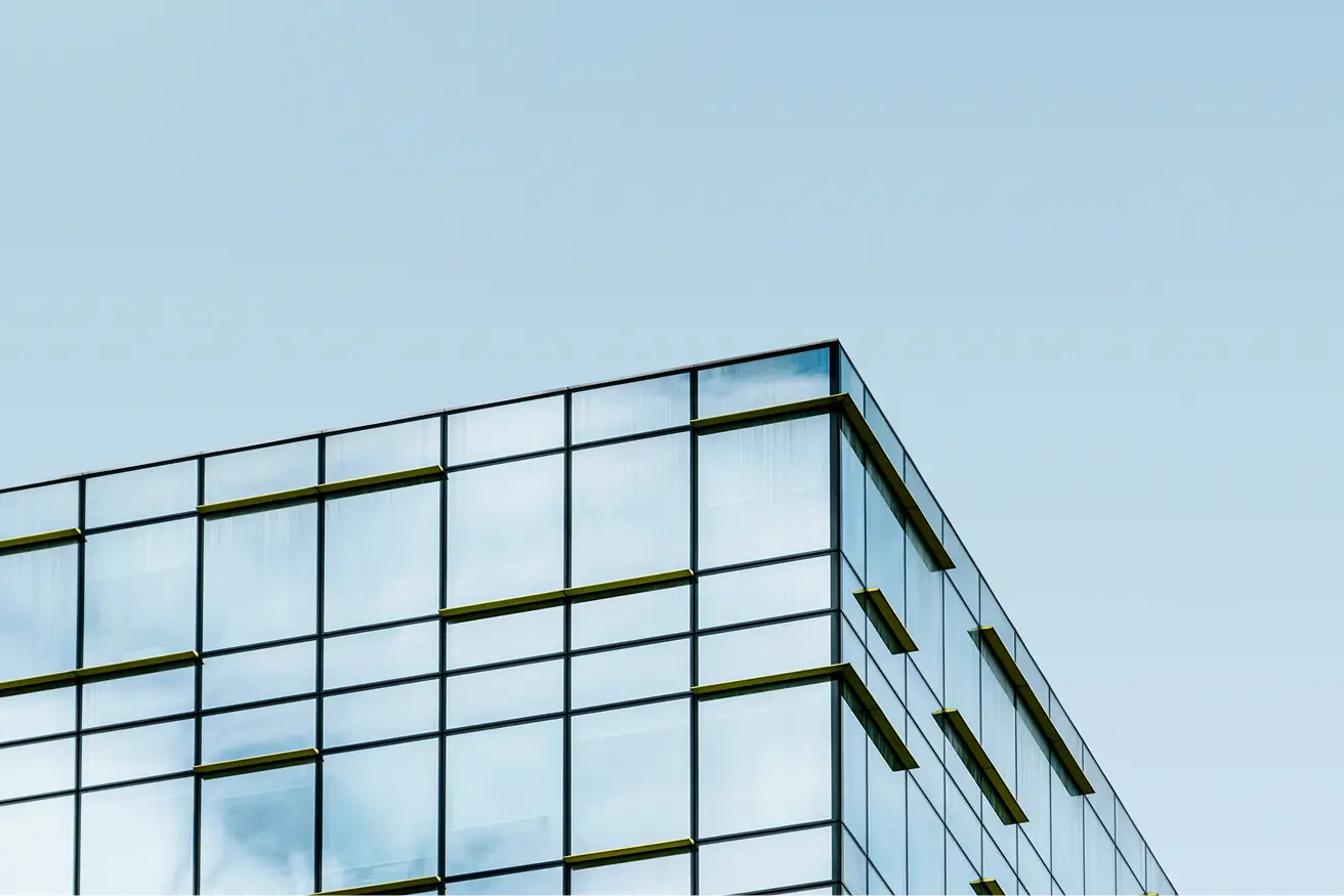 Corner of a modern glass building with reflective windows under a clear blue sky.