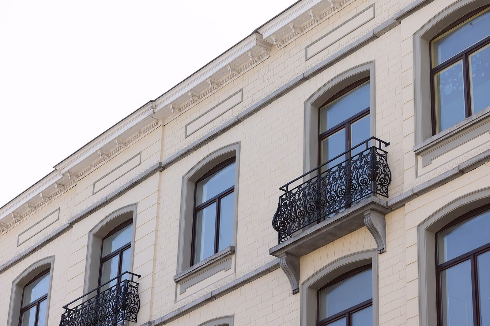 Upper floors of a beige brick building with arched windows and ornate black wrought iron balconies.