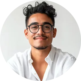 Smiling young man with curly hair, glasses, and a white shirt against a plain light background.