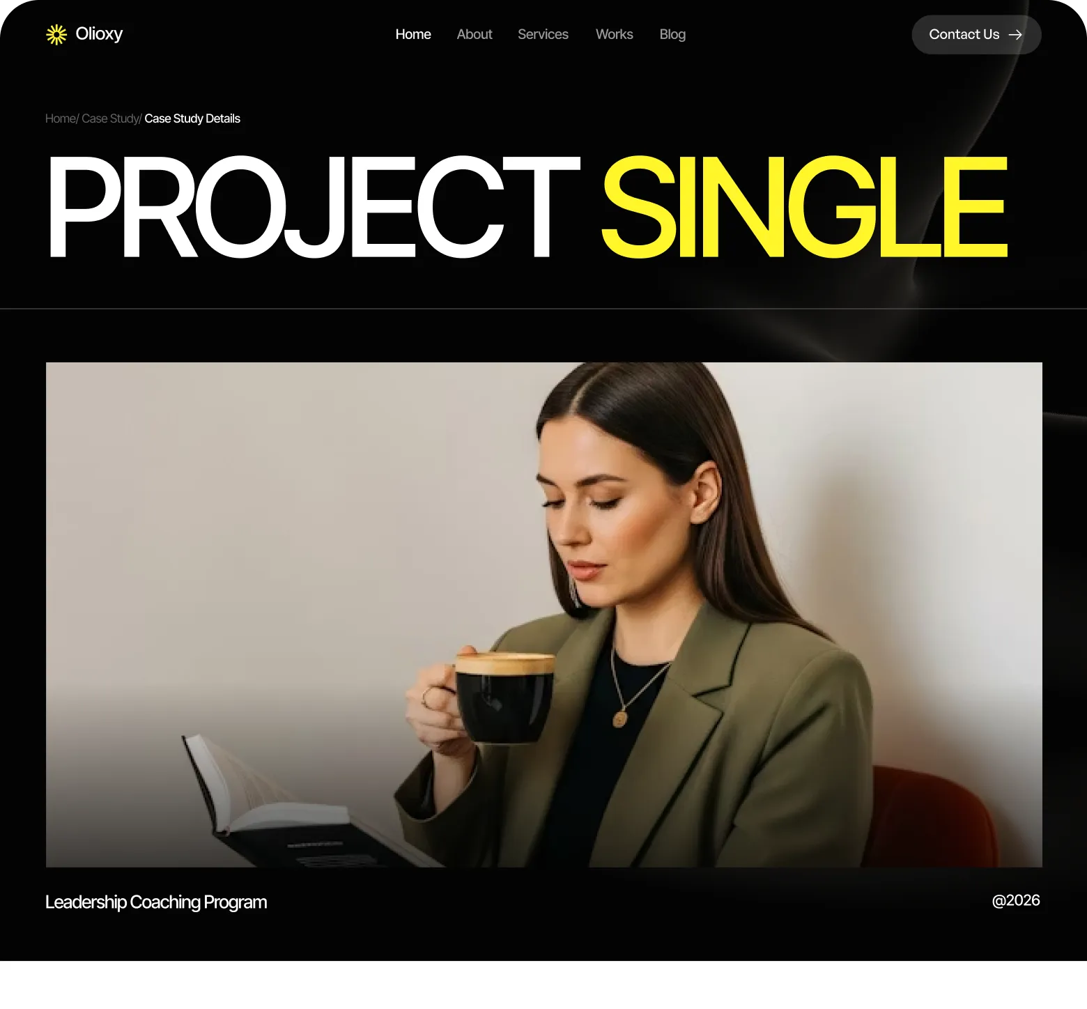 Woman with long brown hair wearing an olive blazer, reading a book and holding a black cup of coffee.