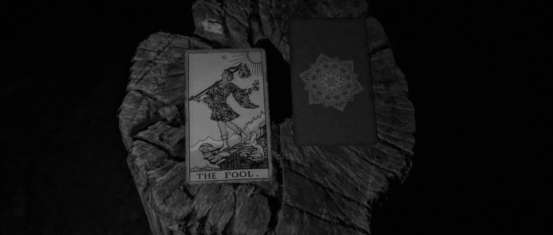 Tarot card The Fool showing a young man with a bag walking near a cliff with a dog on a tree stump.