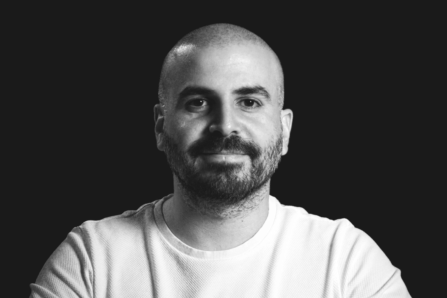 Portrait of a man with a beard wearing a white shirt against a black background.