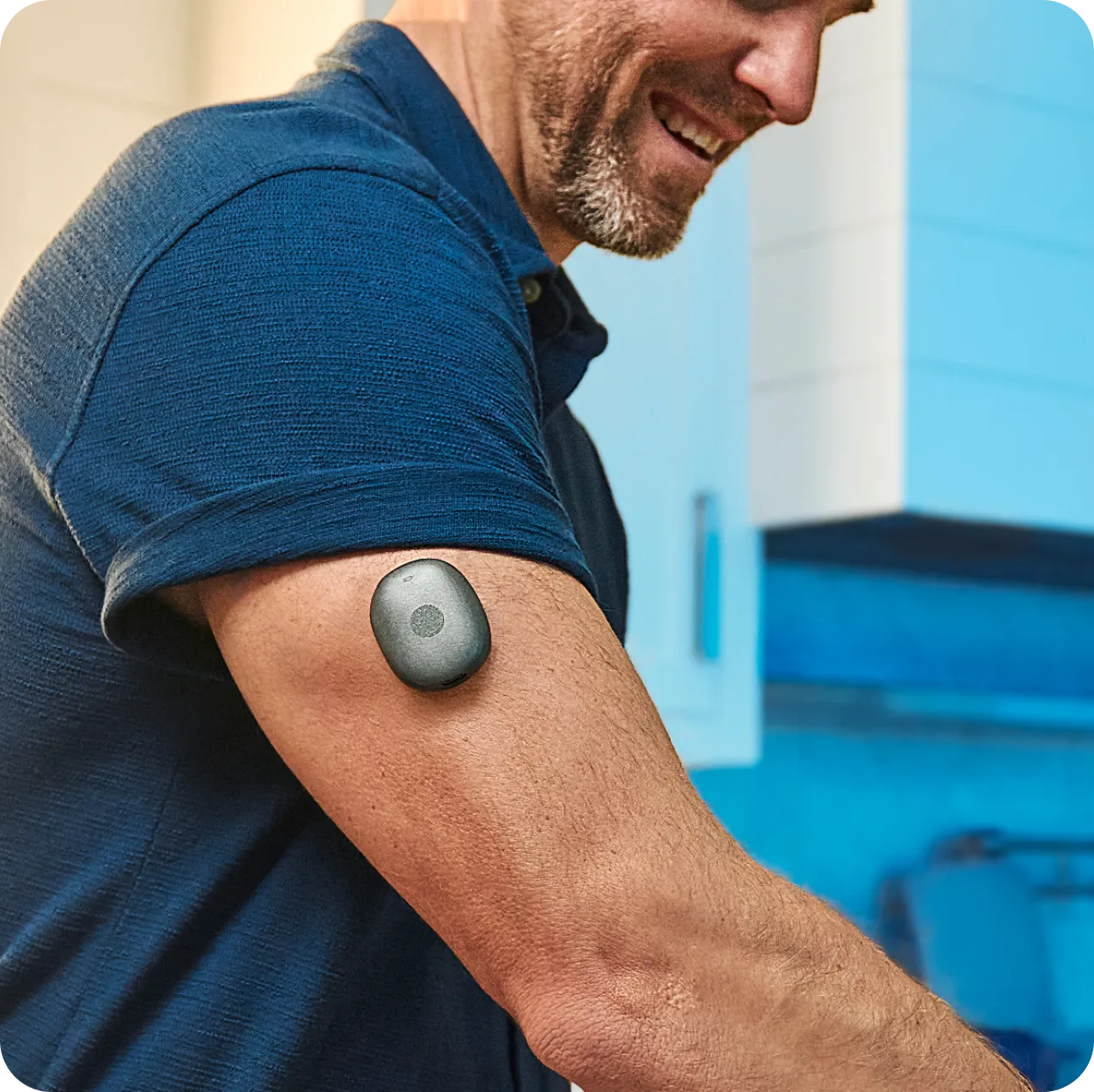 Man smiling wearing a blue shirt with a small gray device attached to his upper arm.