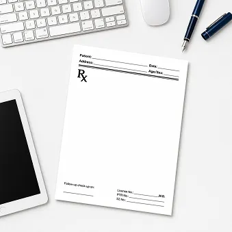 Blank prescription pad on desk with keyboard, tablet, mouse, and pen.