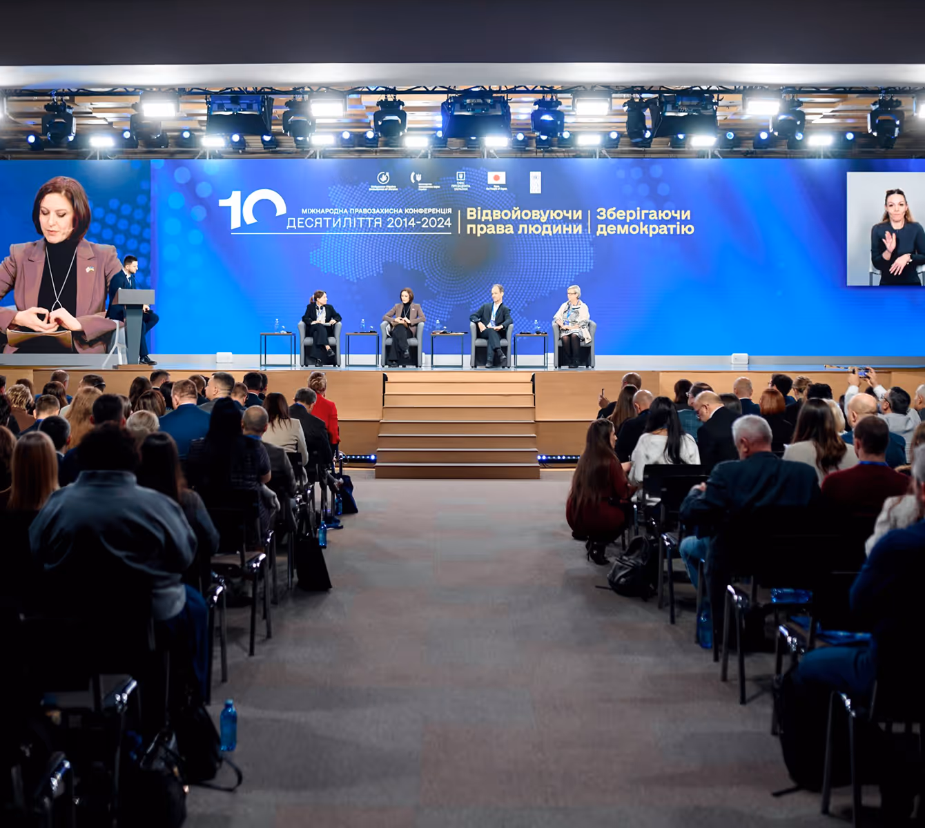 Конференція з прав людини з учасниками на сцені та аудиторією в залі.
