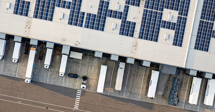 Aerial view of a warehouse loading dock with trucks parked and solar panels installed on the roof.