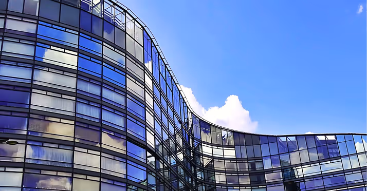 Modern curved glass office building reflecting blue sky with a few white clouds.