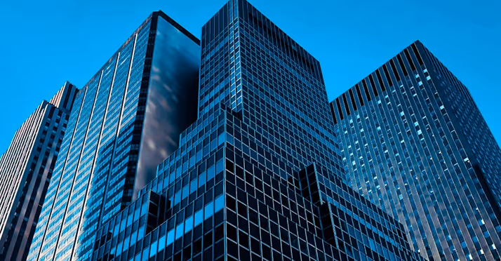 Low-angle view of several modern office skyscrapers with glass facades under a clear blue sky.