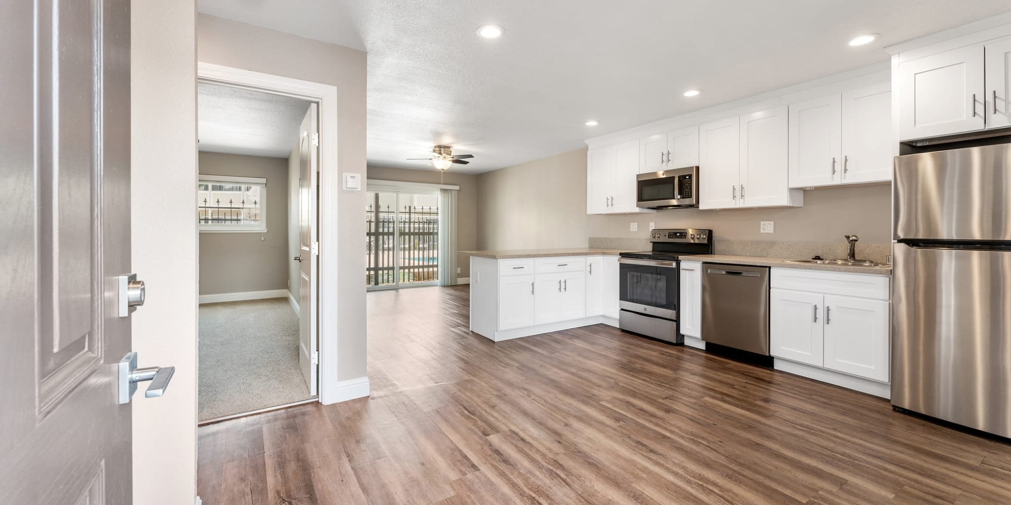 Wide view of unfurnished living and dining area with view of kitchen with white cabinets and stainless steel appliances