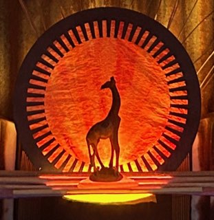 Silhouette of a giraffe statue in front of a large circular orange and black decorative backdrop.