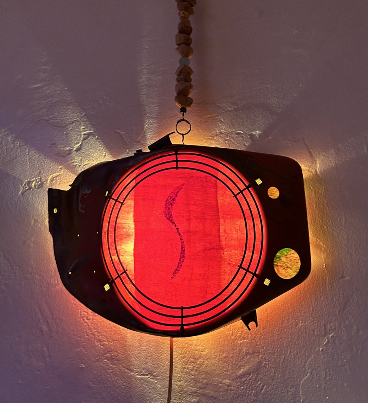 Vintage red circular wall light with a metal frame casting a warm glow on a textured wall.