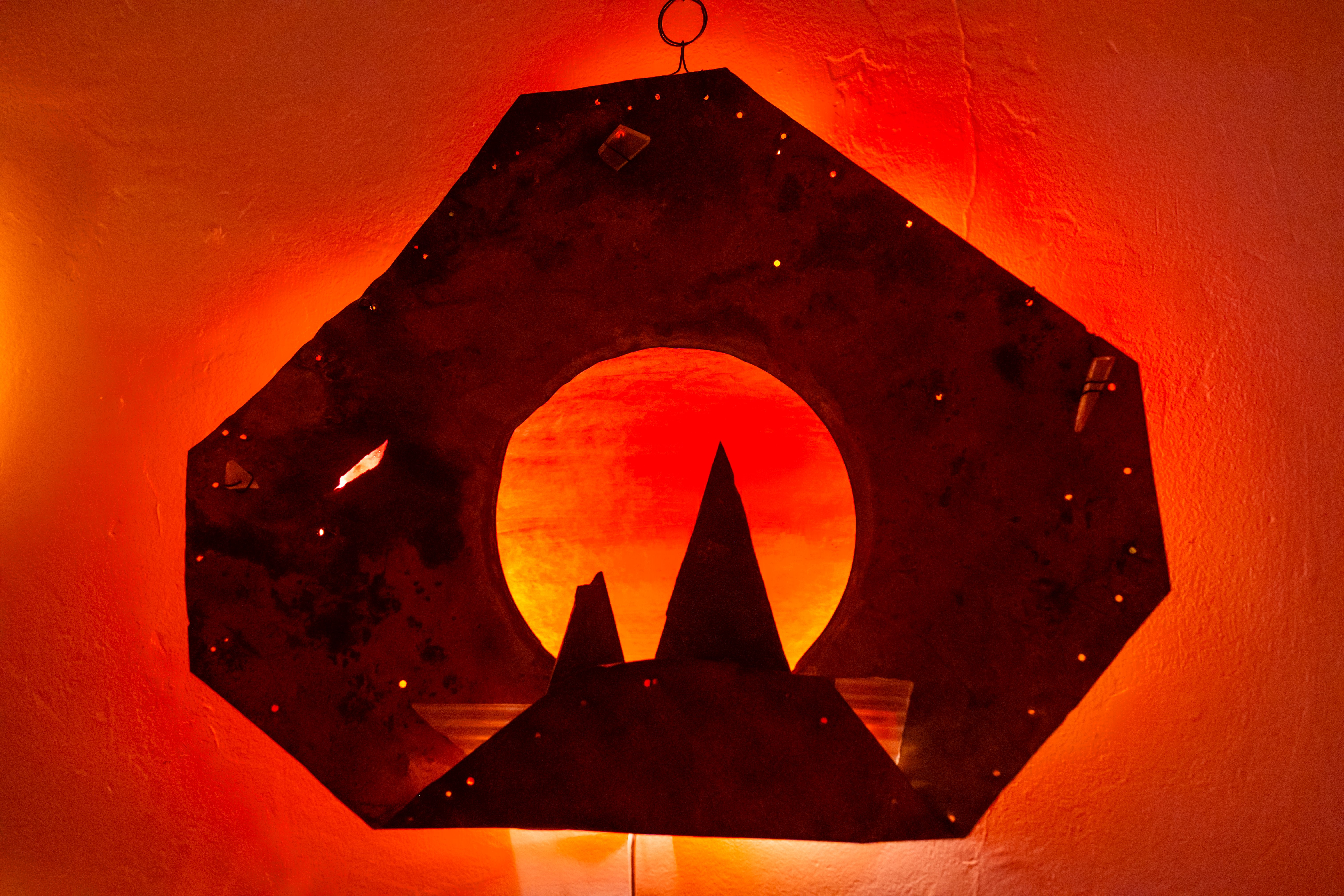 Wall lamp with red-orange glow and a metal frame shaped like mountains and a sun.