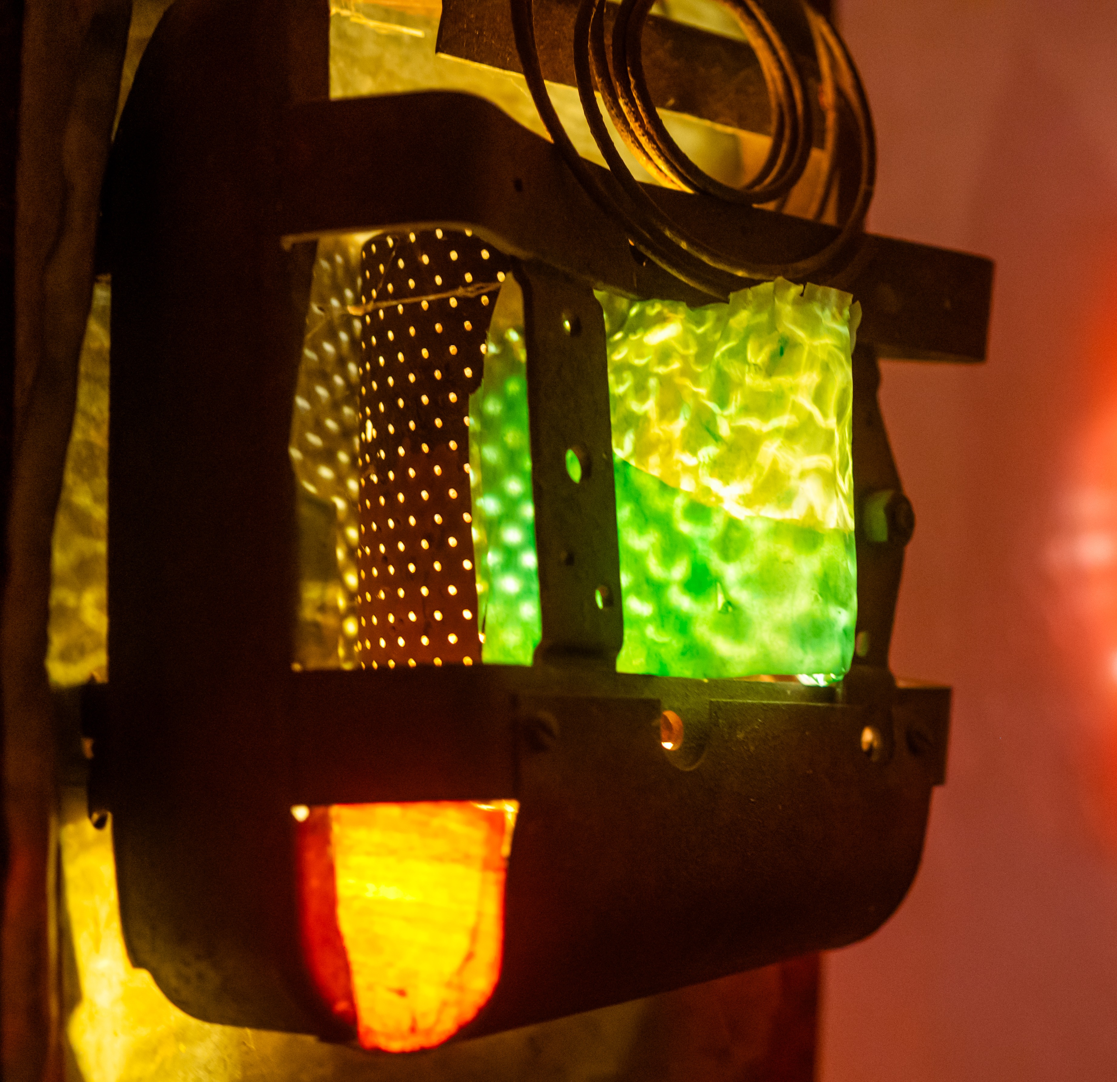Close-up of a decorative lantern with green, yellow, and orange glowing panels and metal frame.