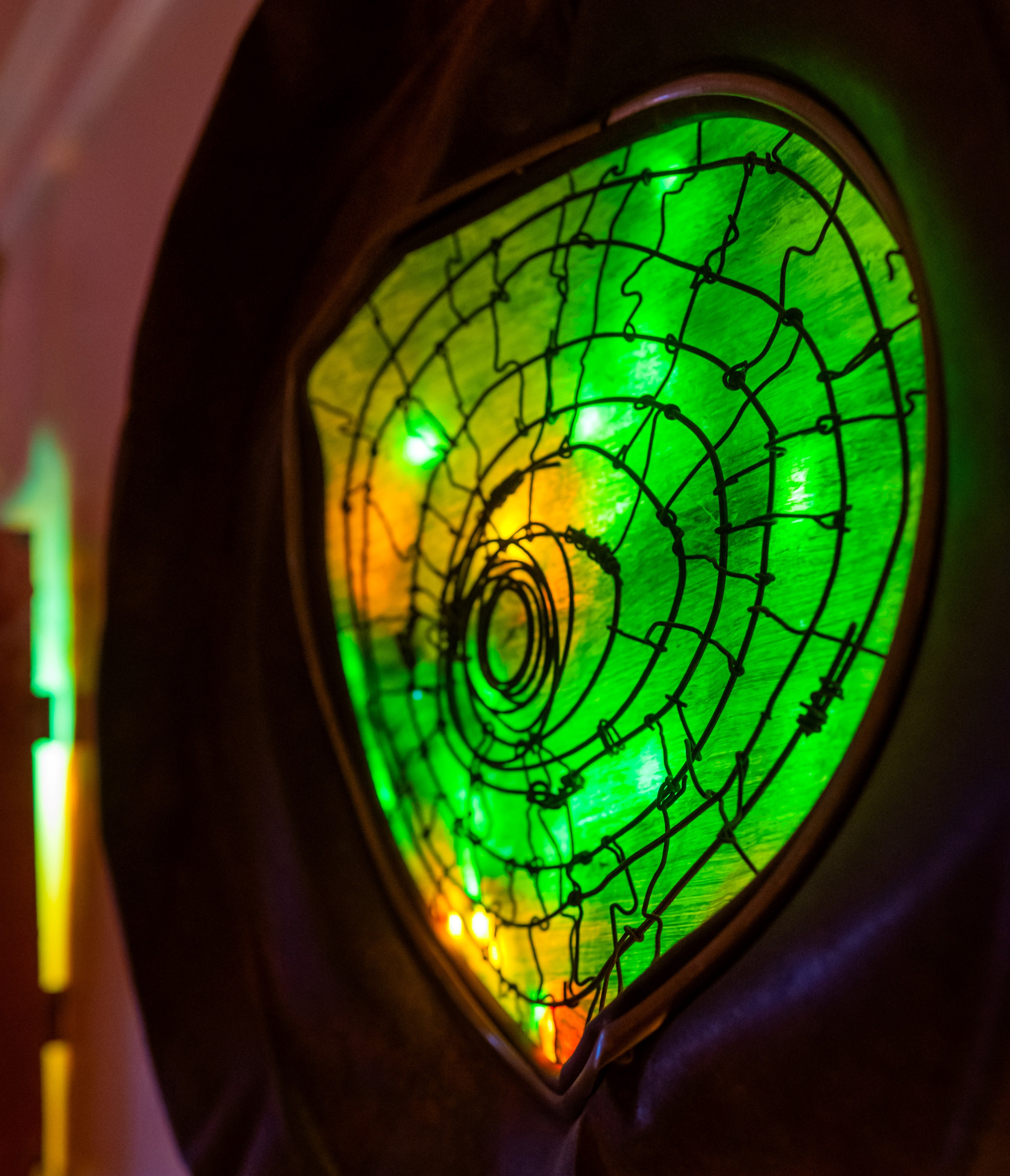 Close-up of a stained glass window glowing with green and yellow light, outlined by black wire design.