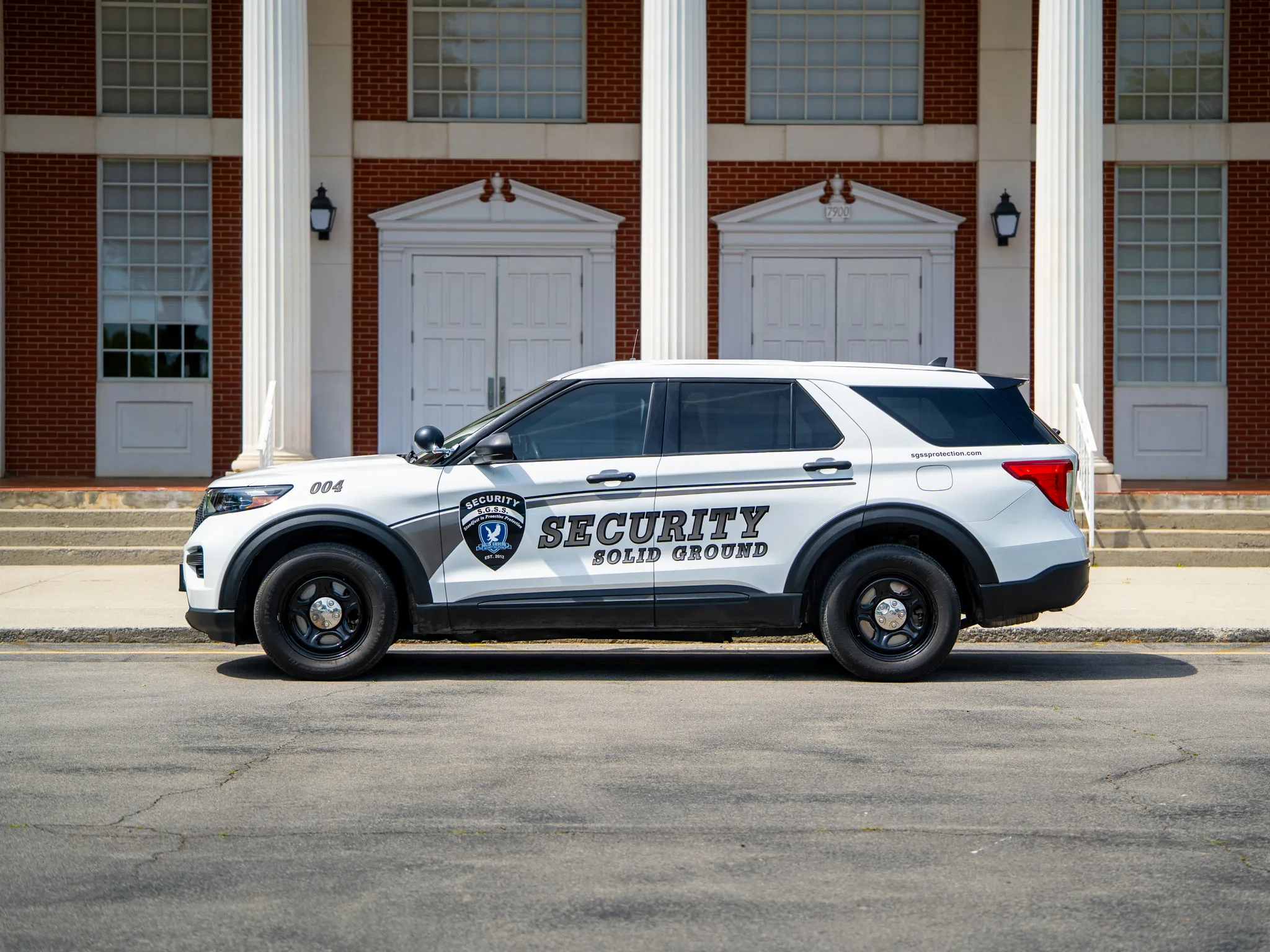 White security SUV with Solid Ground Security logo parked in front of a brick building with columns.