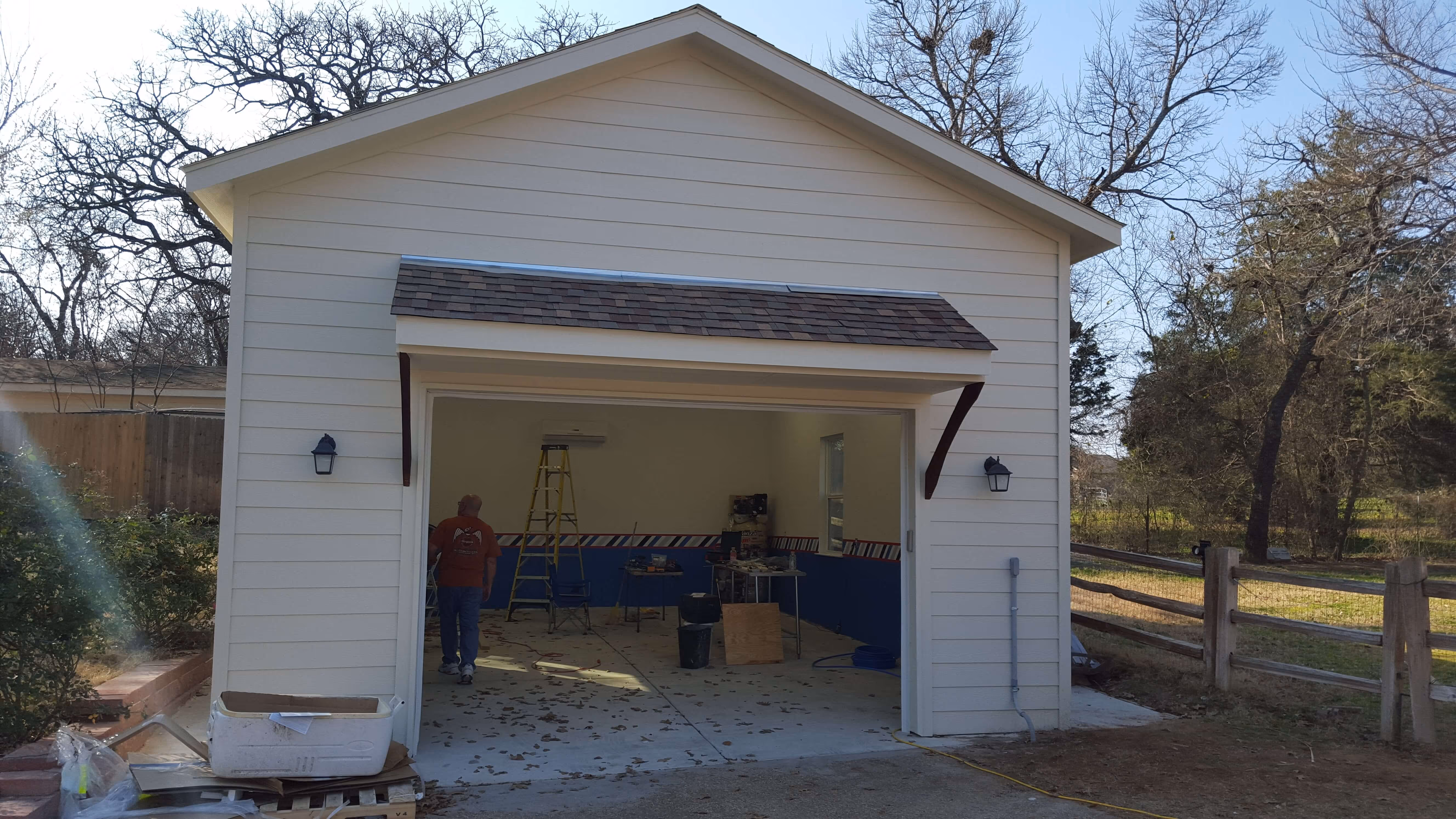White garage under construction with open door, ladder, tools, and a person inside walking away.