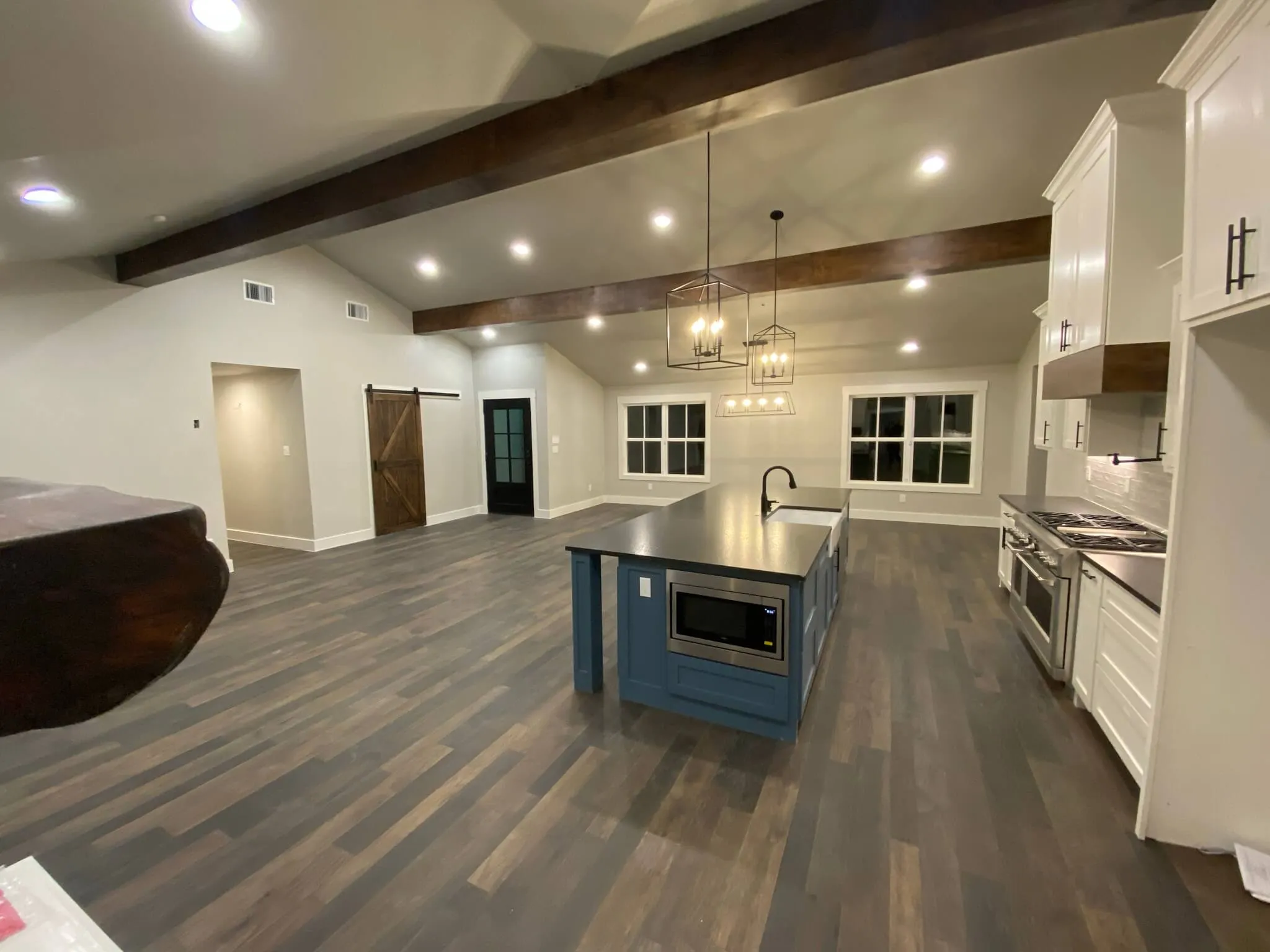 Open kitchen with blue island, dark wood floors, white cabinets, and exposed wood ceiling beams.
