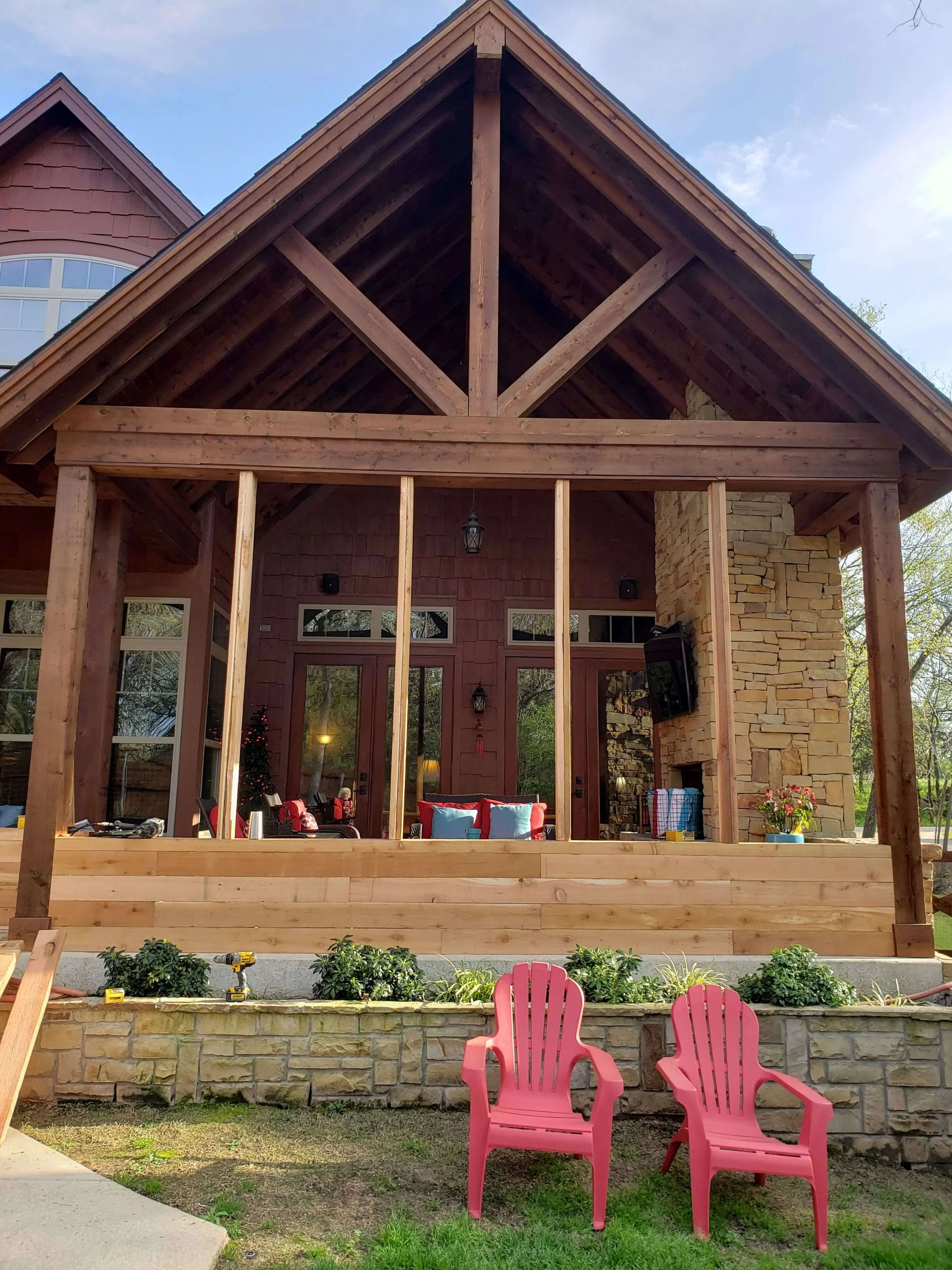 Wooden porch under construction with two red chairs on lawn in front of stone retaining wall.