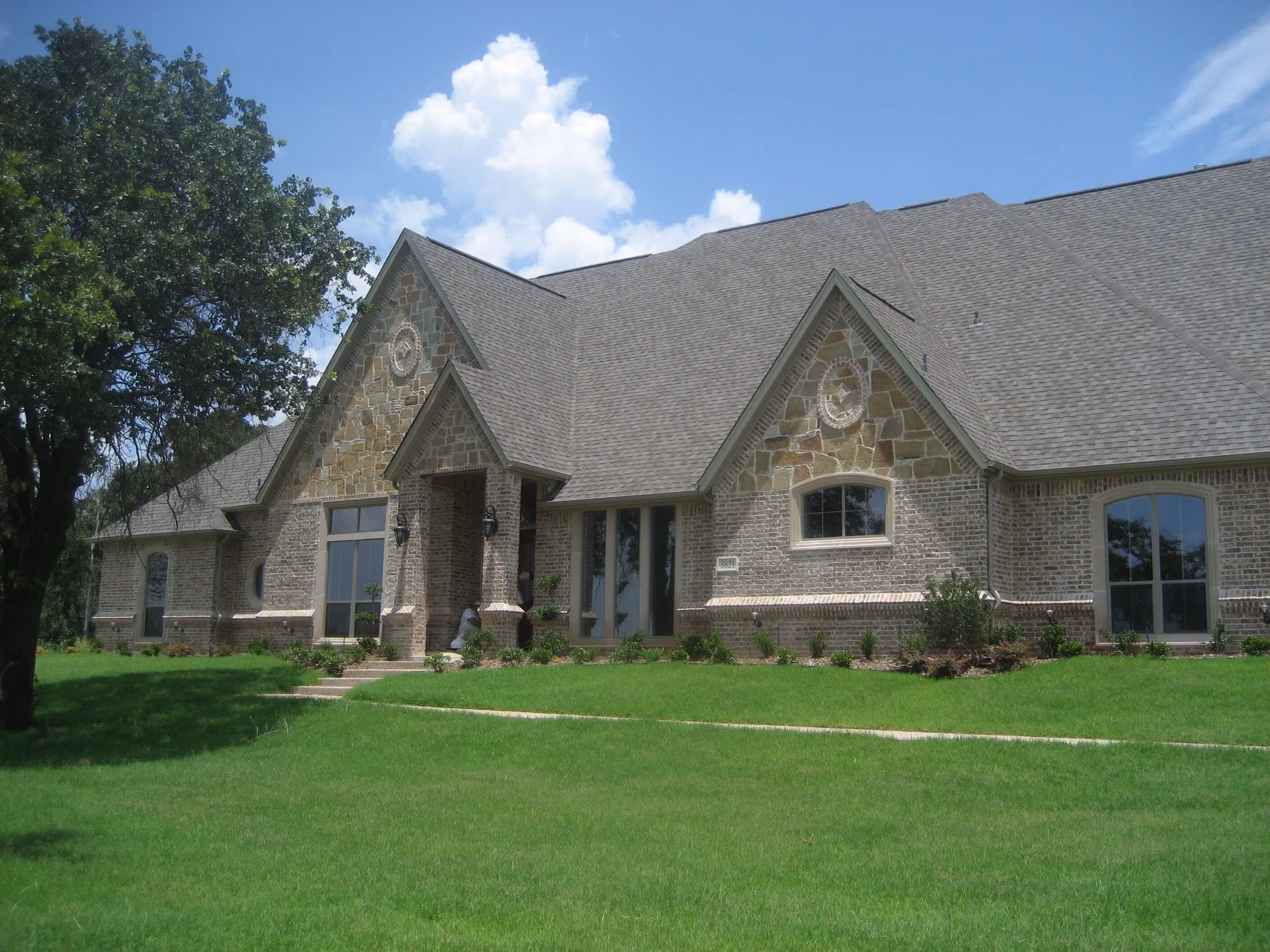 Large brick and stone house with steep gabled roof and green lawn under a blue sky.
