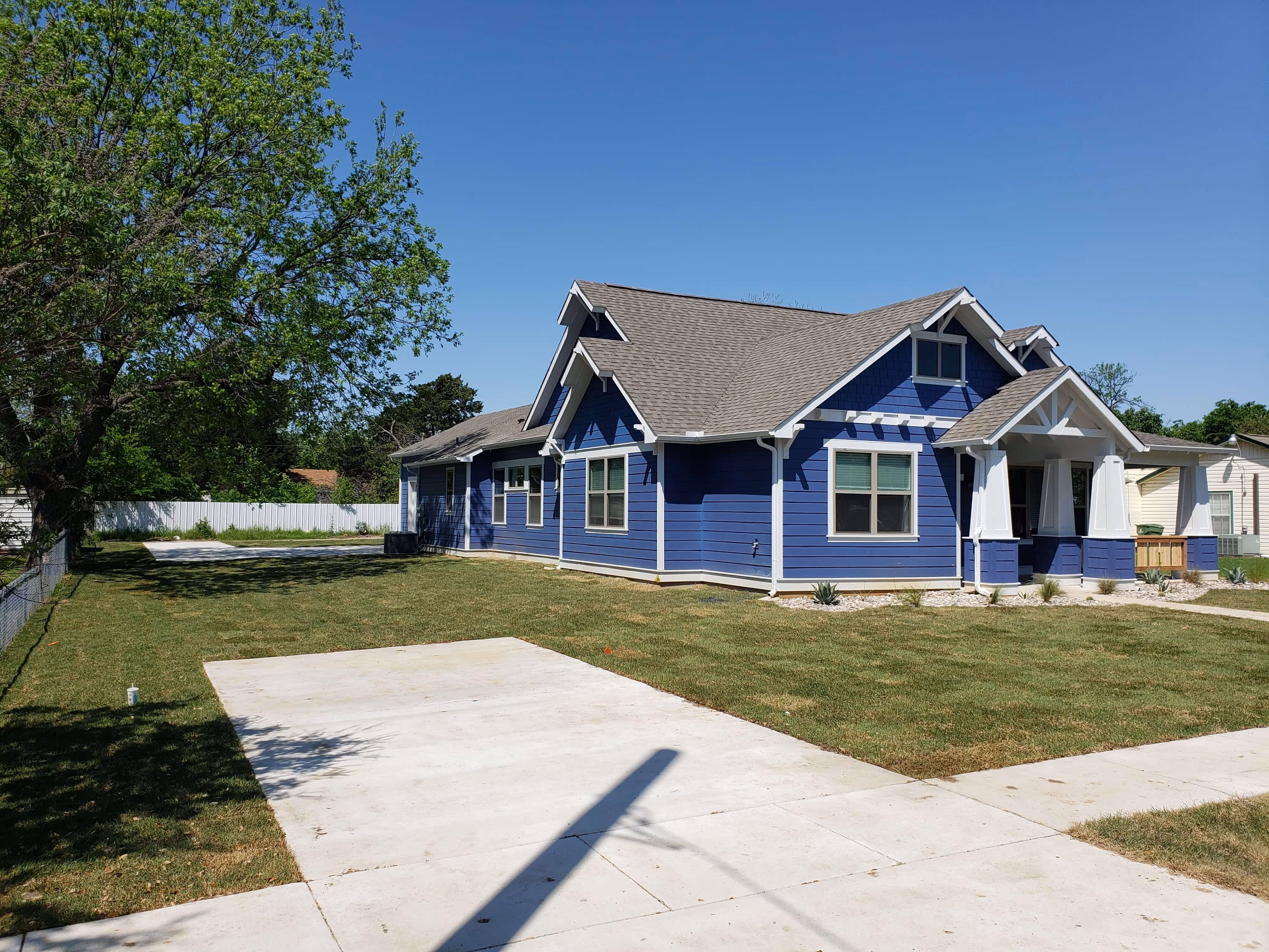 Single-story blue house with white trim, green lawn, tree on left, and clear blue sky.