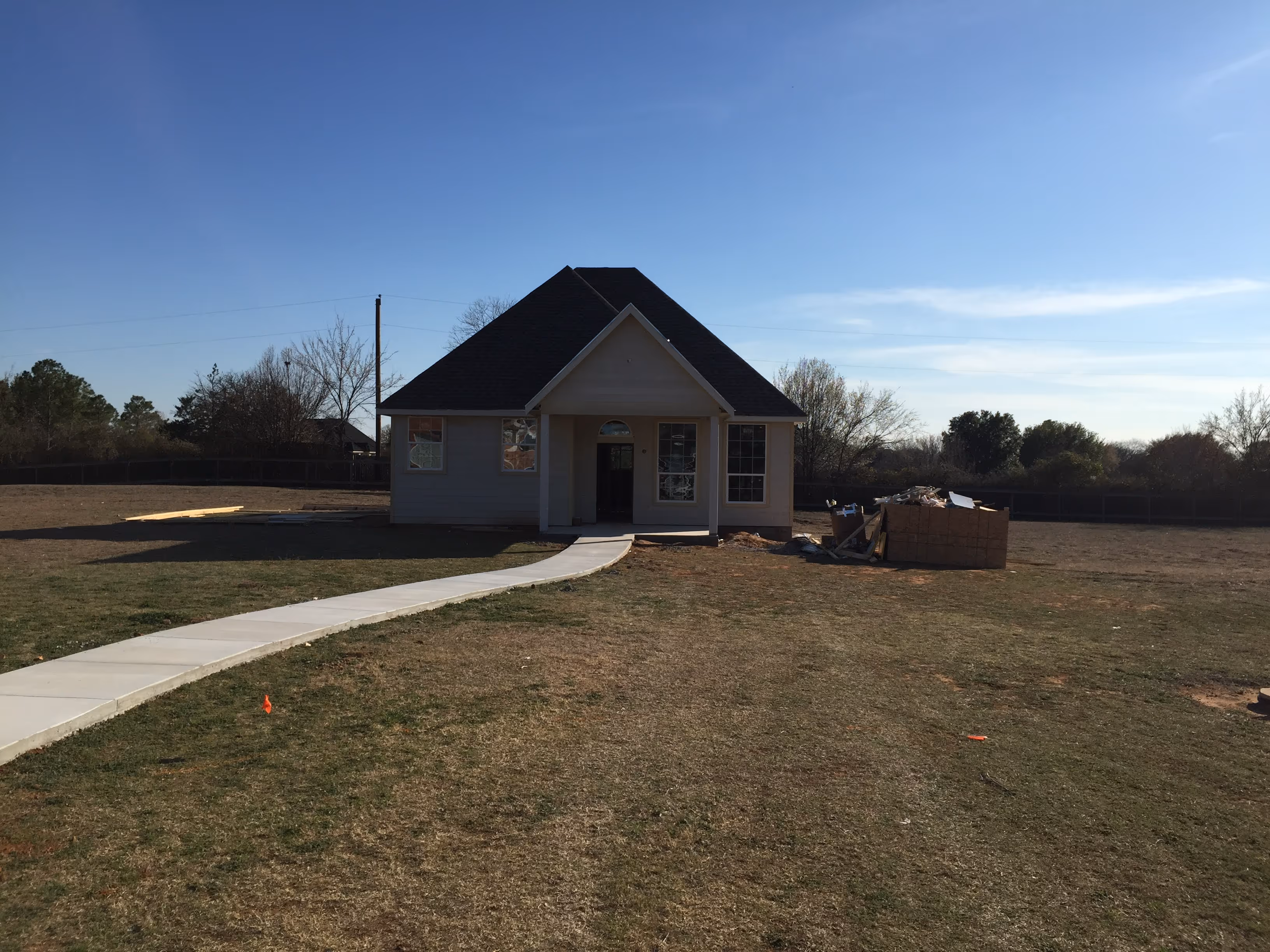 New house with dark roof and white walls at the end of a winding concrete path on a grassy lawn.