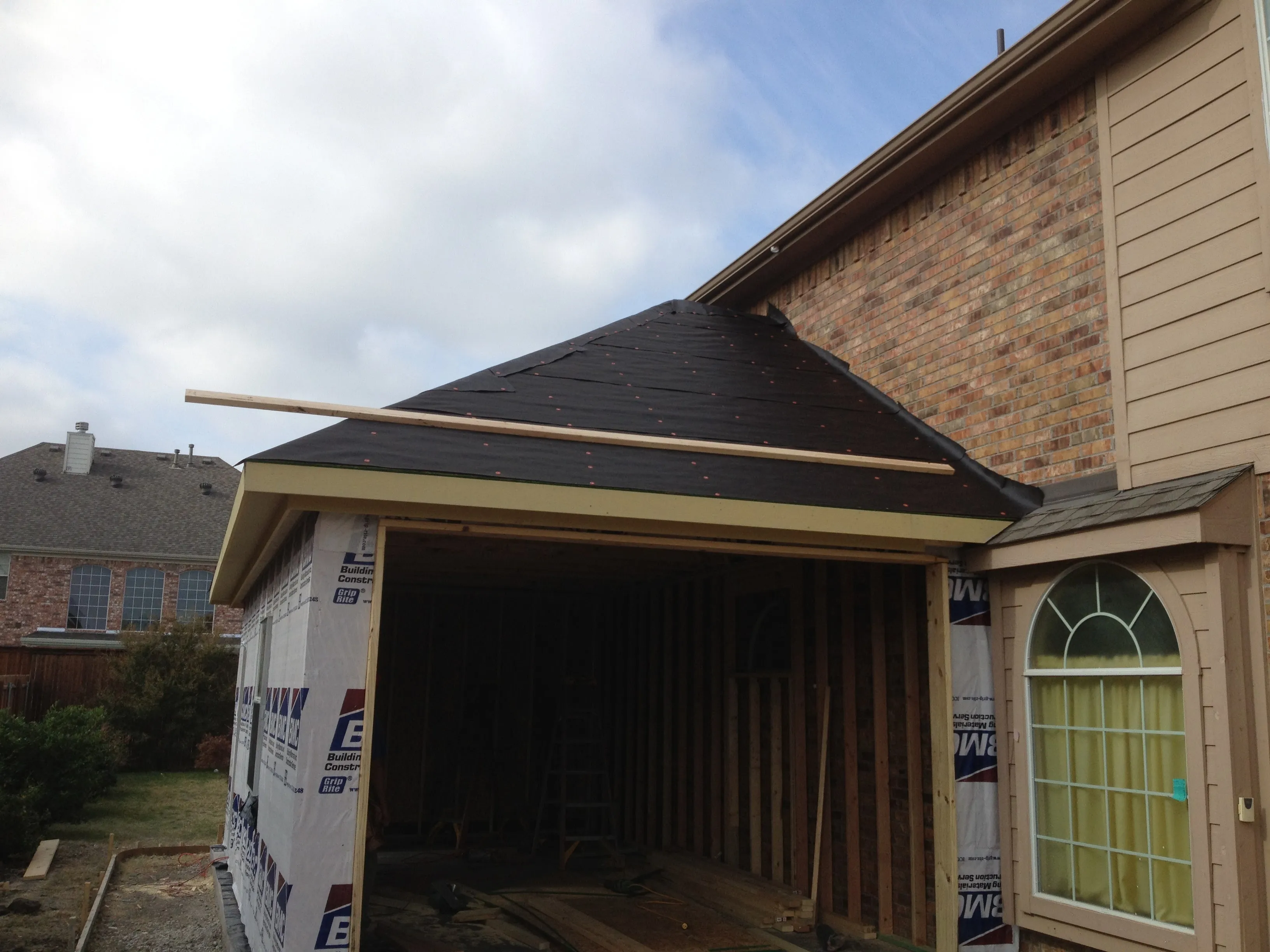 New construction attached garage with framed walls and black roofing underlayment on the roof.