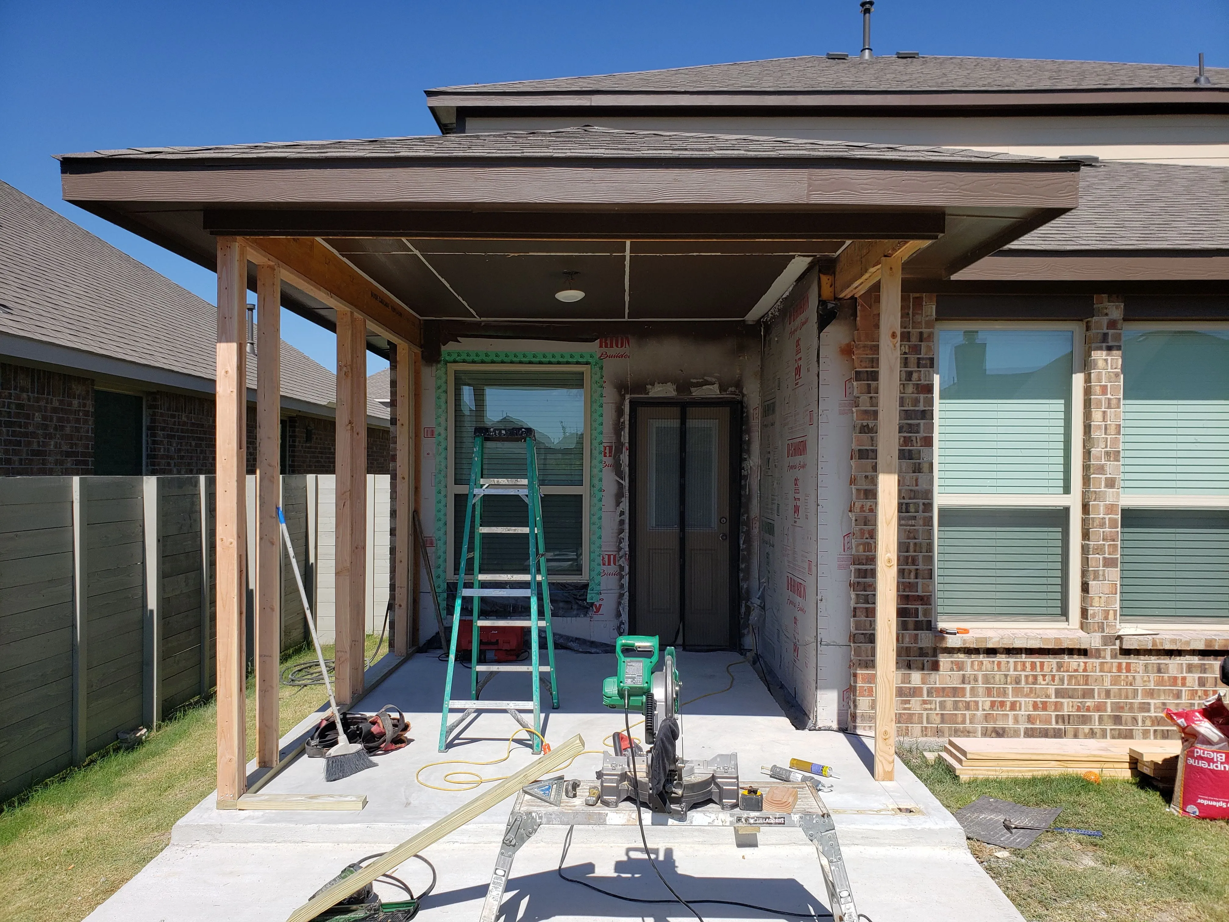 Home porch under construction with wooden frame, ladder, and power saw on concrete floor.