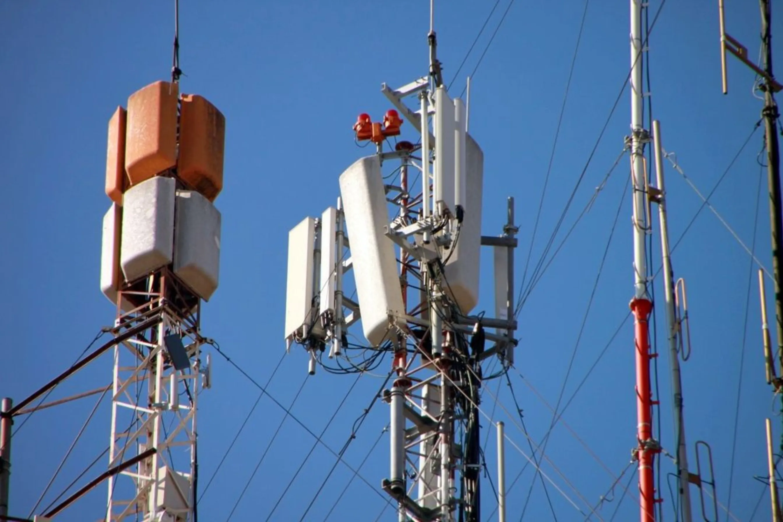Close-up of multiple telecommunications antennas and equipment on metal towers against a blue sky.