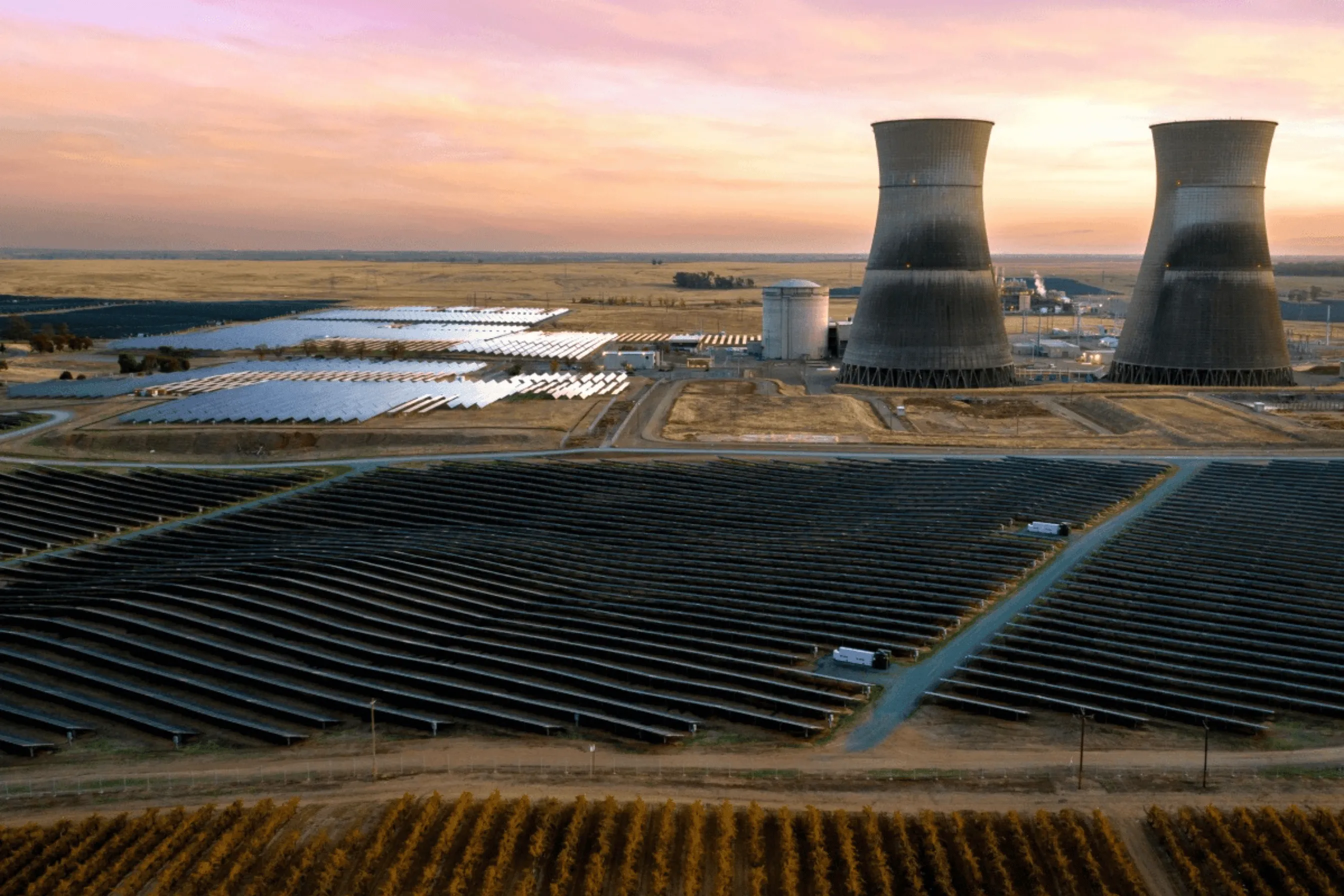 Large solar panel fields and cooling towers of a power plant at sunset.