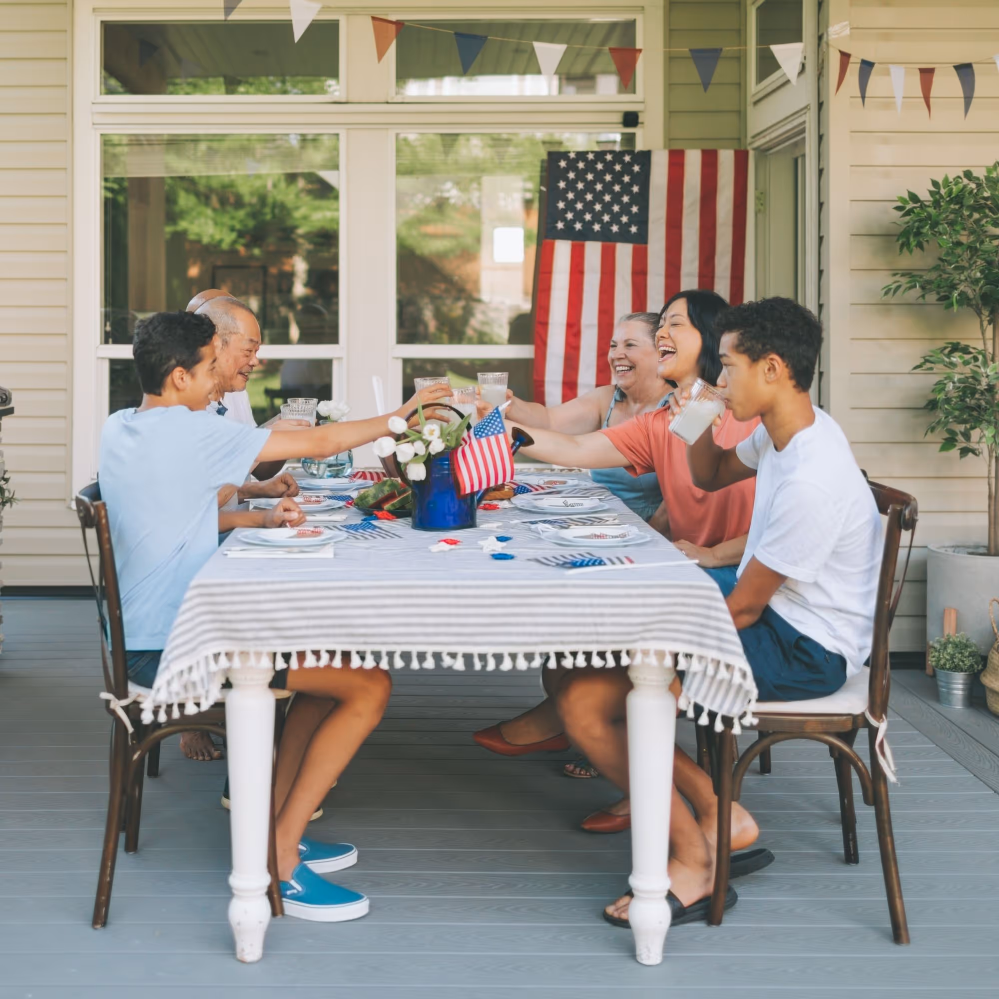 Multigenerational family toasting drinks at a decorated outdoor table with an American flag.