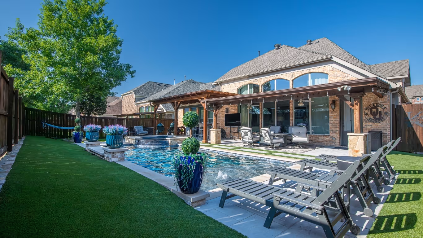 Modern backyard with a rectangular pool, lounge chairs, covered patio, and plants in blue pots.