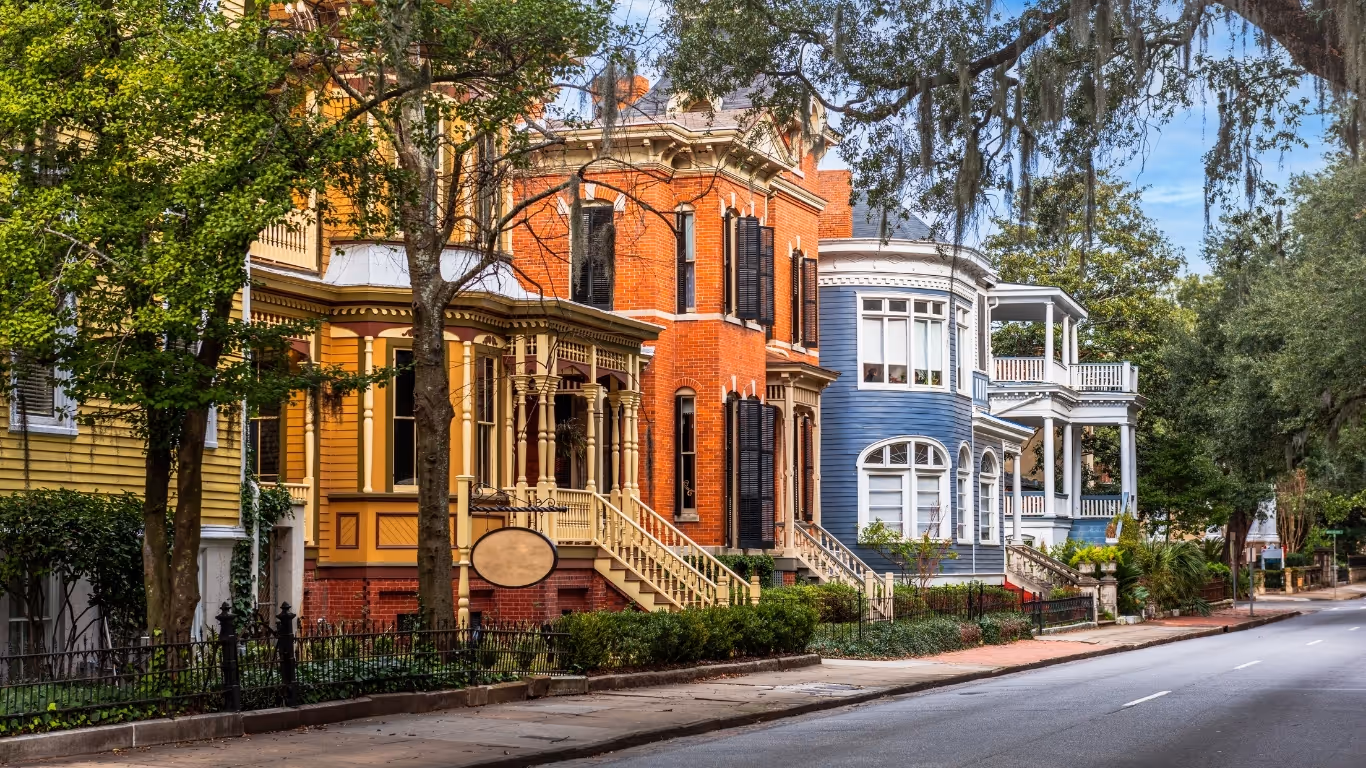 Colorful historic houses with porches along a tree-lined street in Savannah, Georgia.