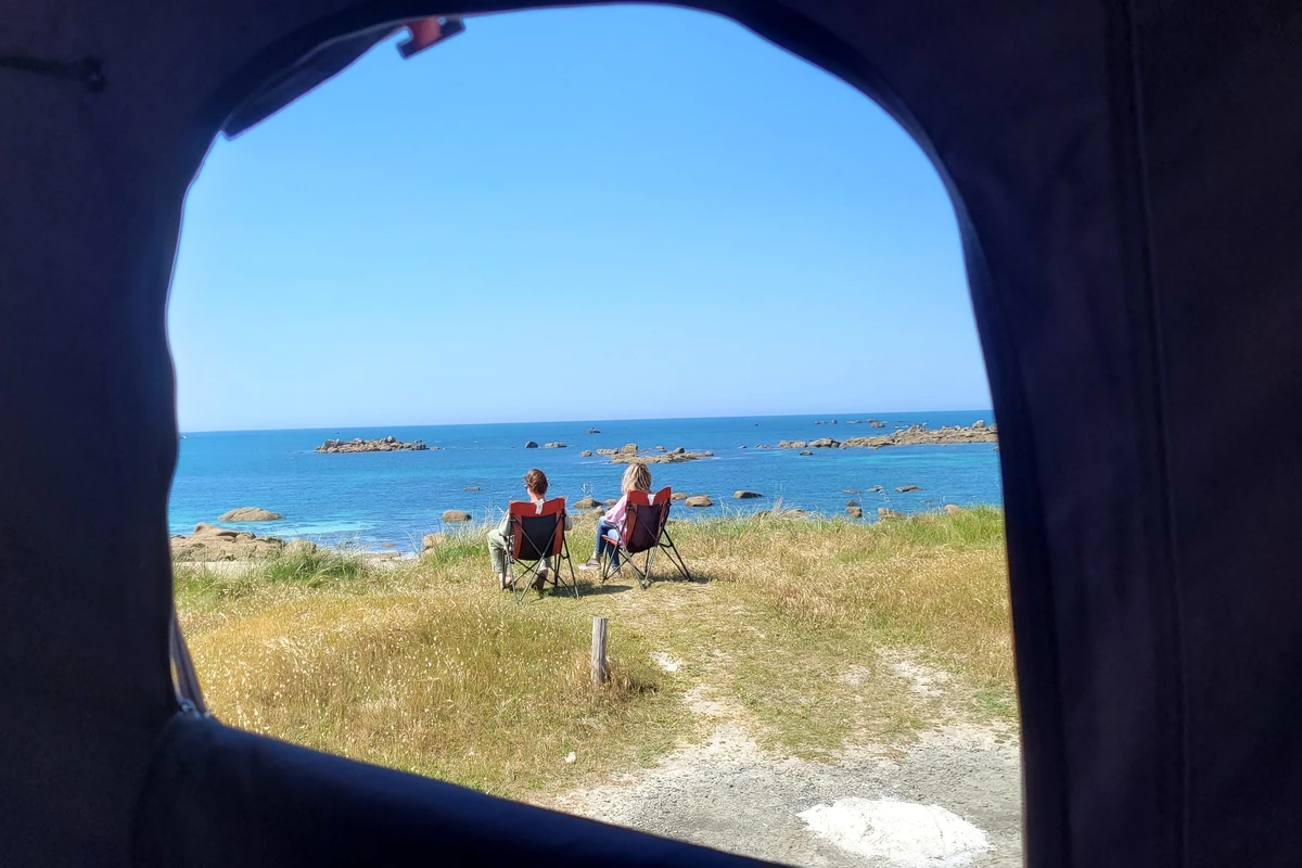 Vue depuis l'intérieur de la tente iKamper sur un couple face à l'océan et aux rochers bretons