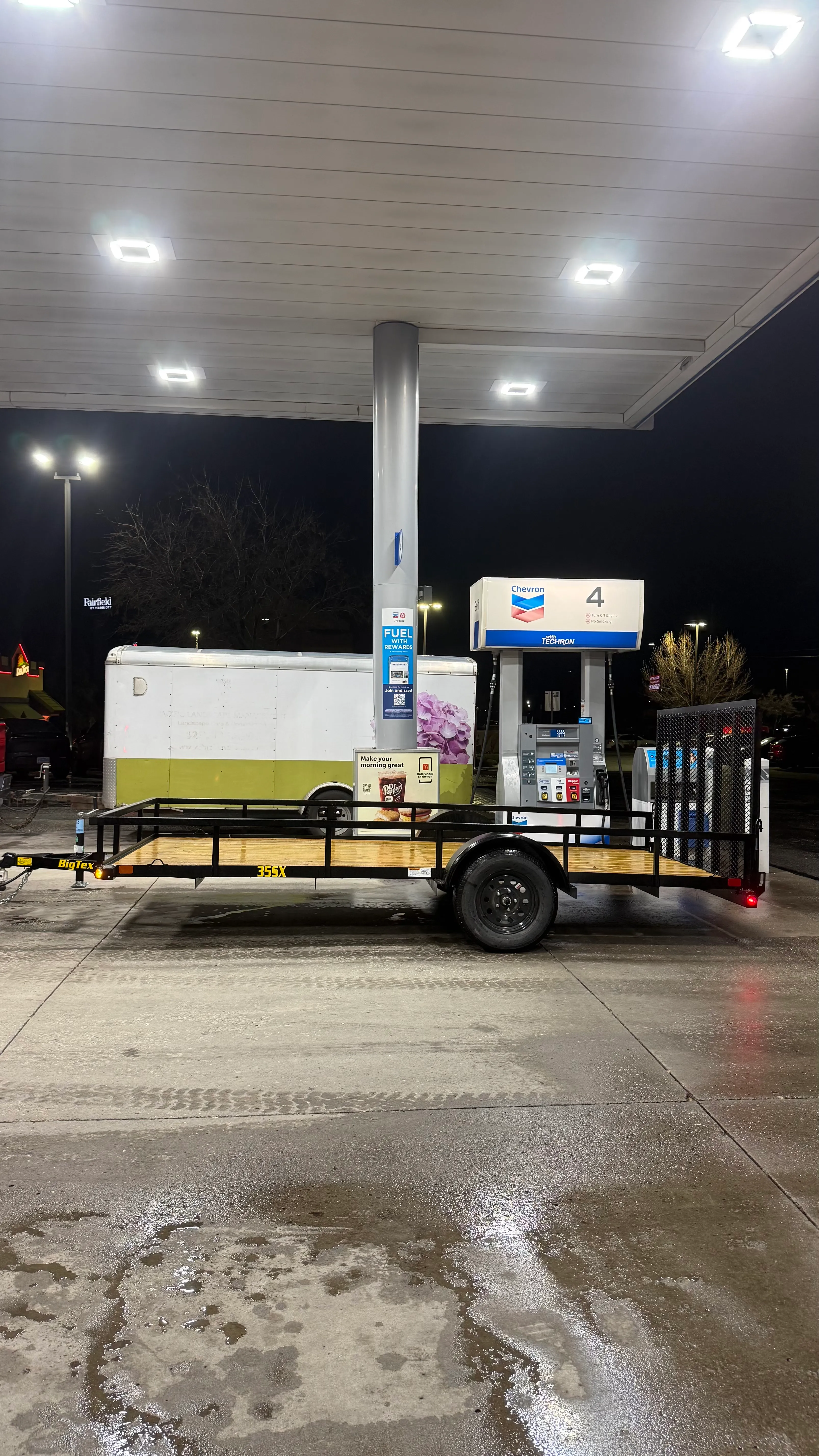 Empty black flatbed trailer parked at a Chevron gas station pump at night.