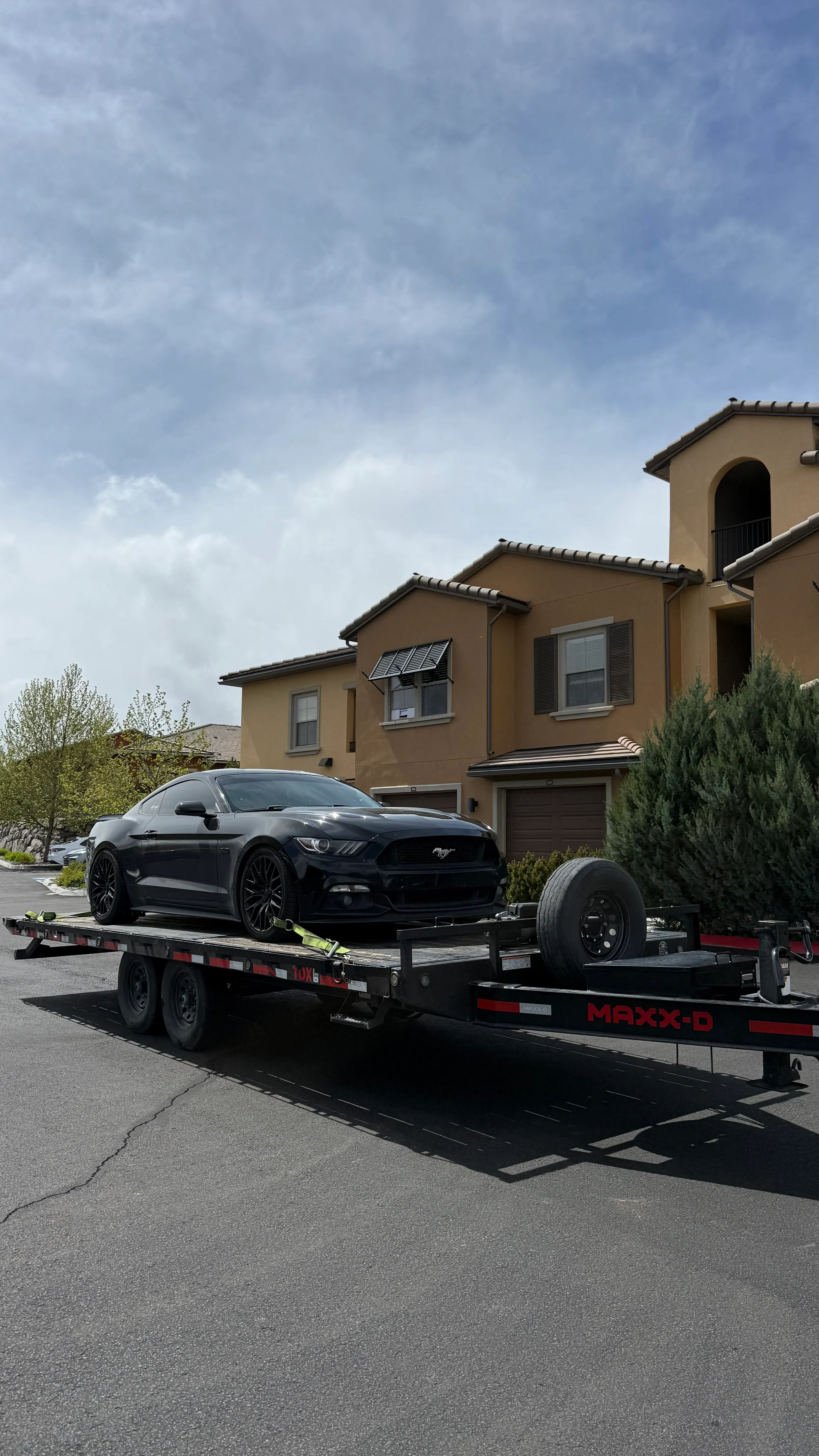 Black Mustang GT strapped on a car trailer on a suburban street
