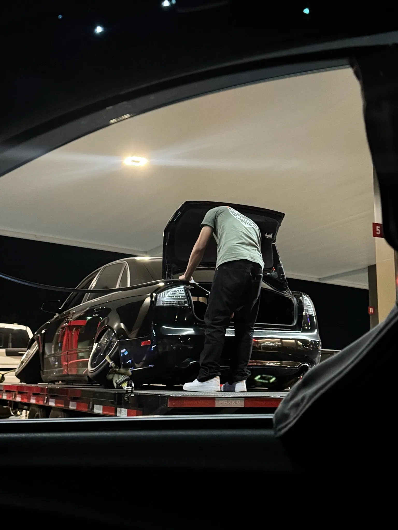 Andrew, owner of OTG Trailer Rentals, checking a lowered black car strapped on a trailer at night